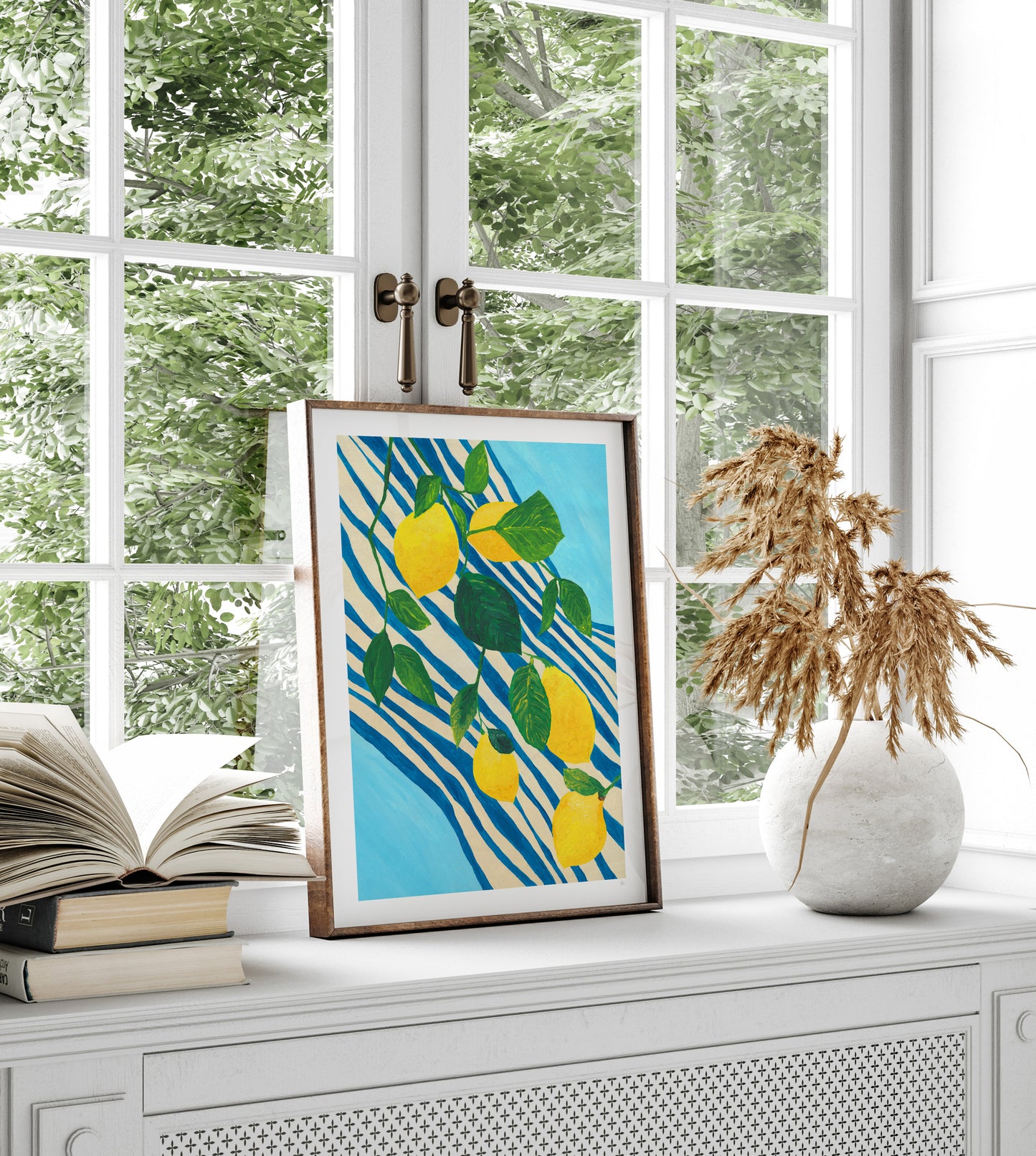 Framed artwork with lemons on a window sill with books and a vase.