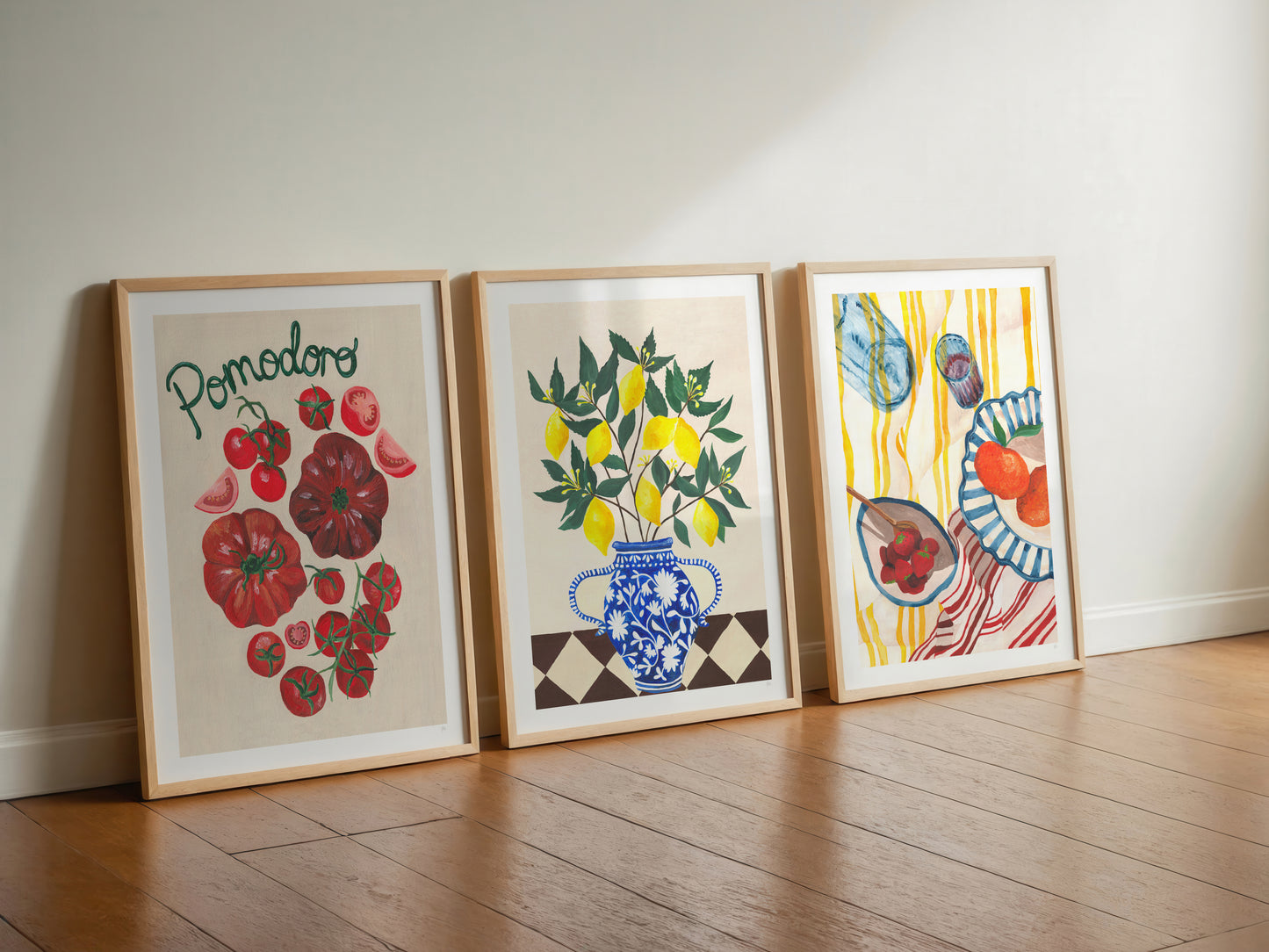 Three framed artworks on a wooden floor against a white wall