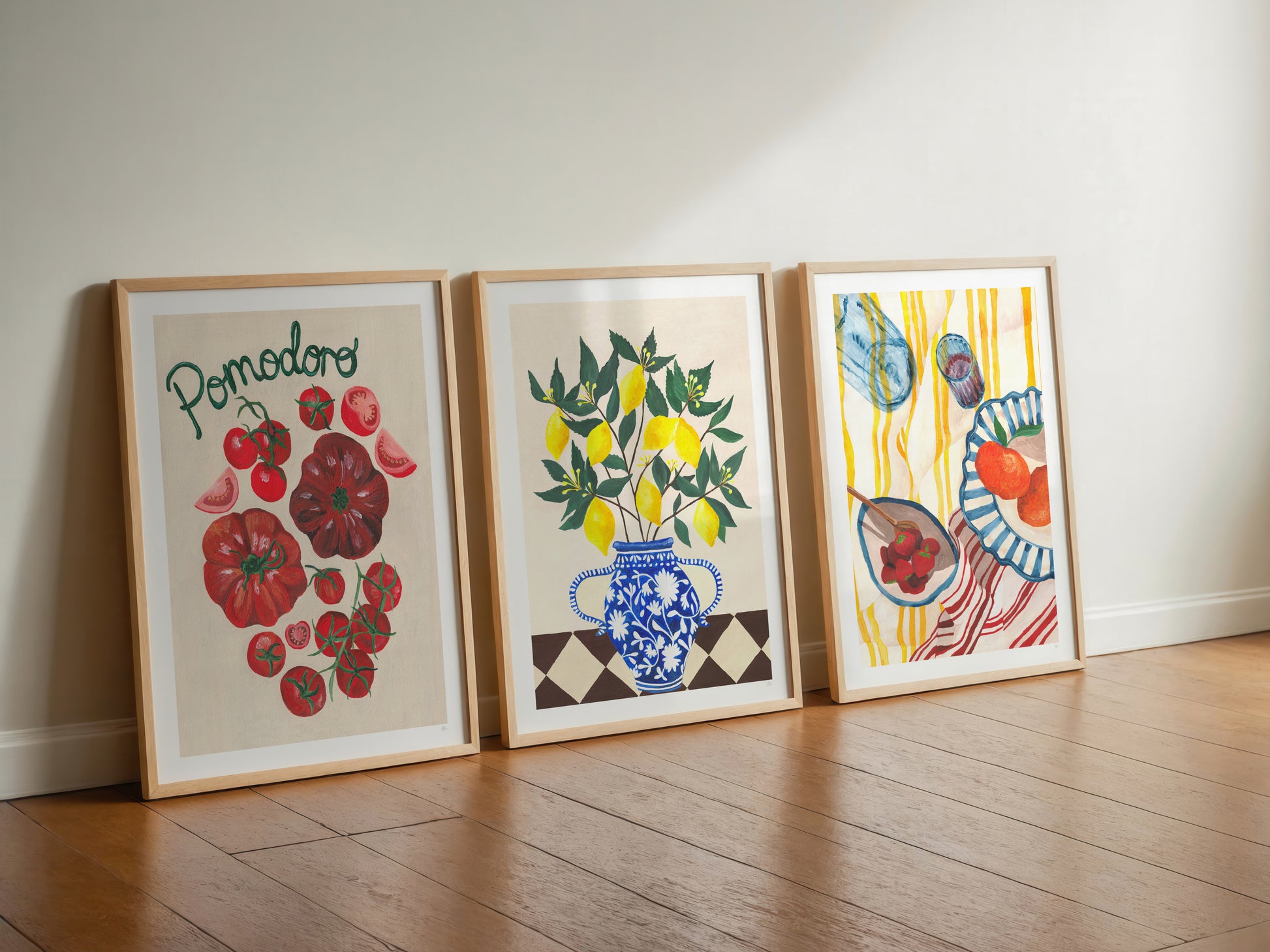 Three framed artworks on a wooden floor against a white wall