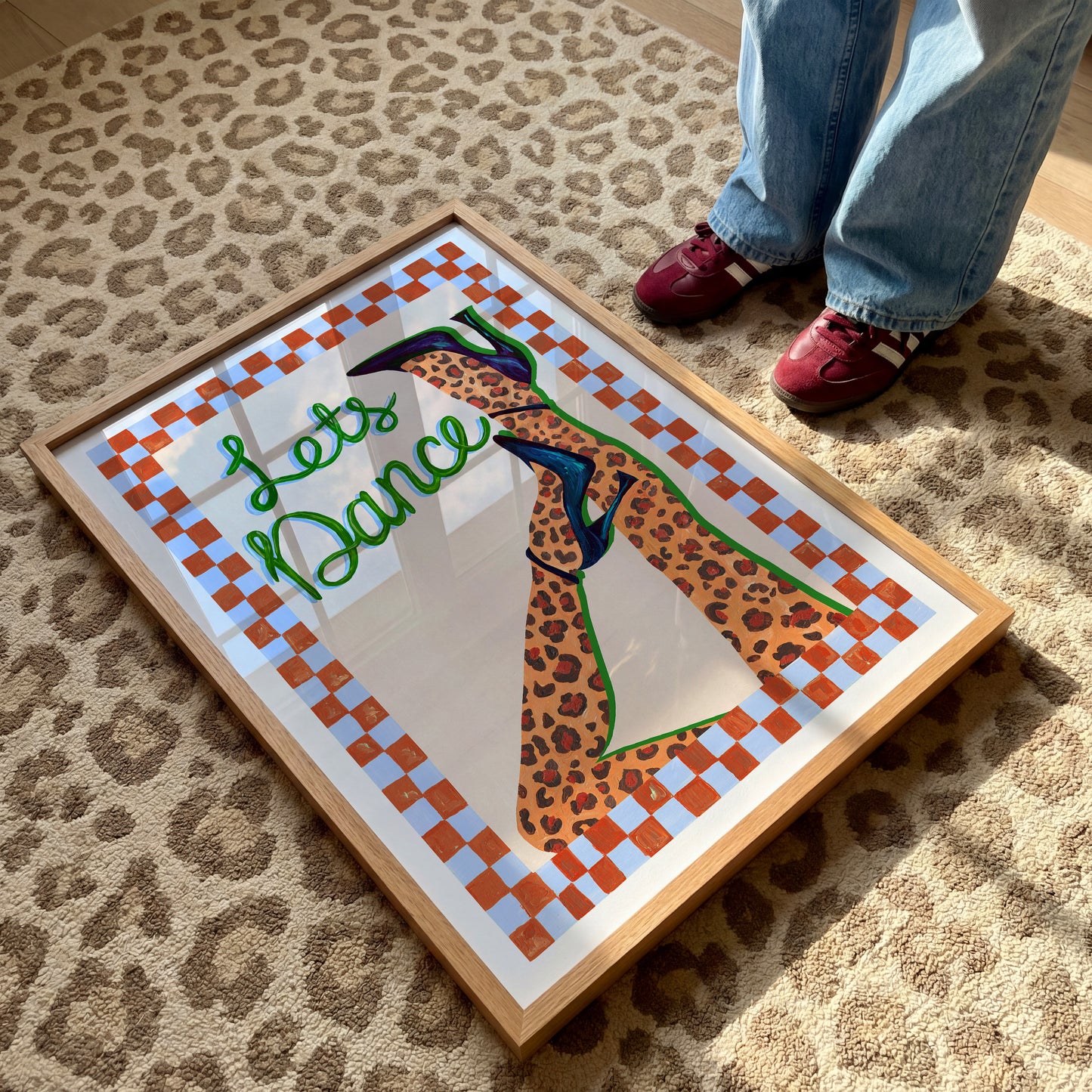 Framed artwork with a leopard print dancer and 'Let's Dance' text on a checkered background, placed on a leopard print carpet.