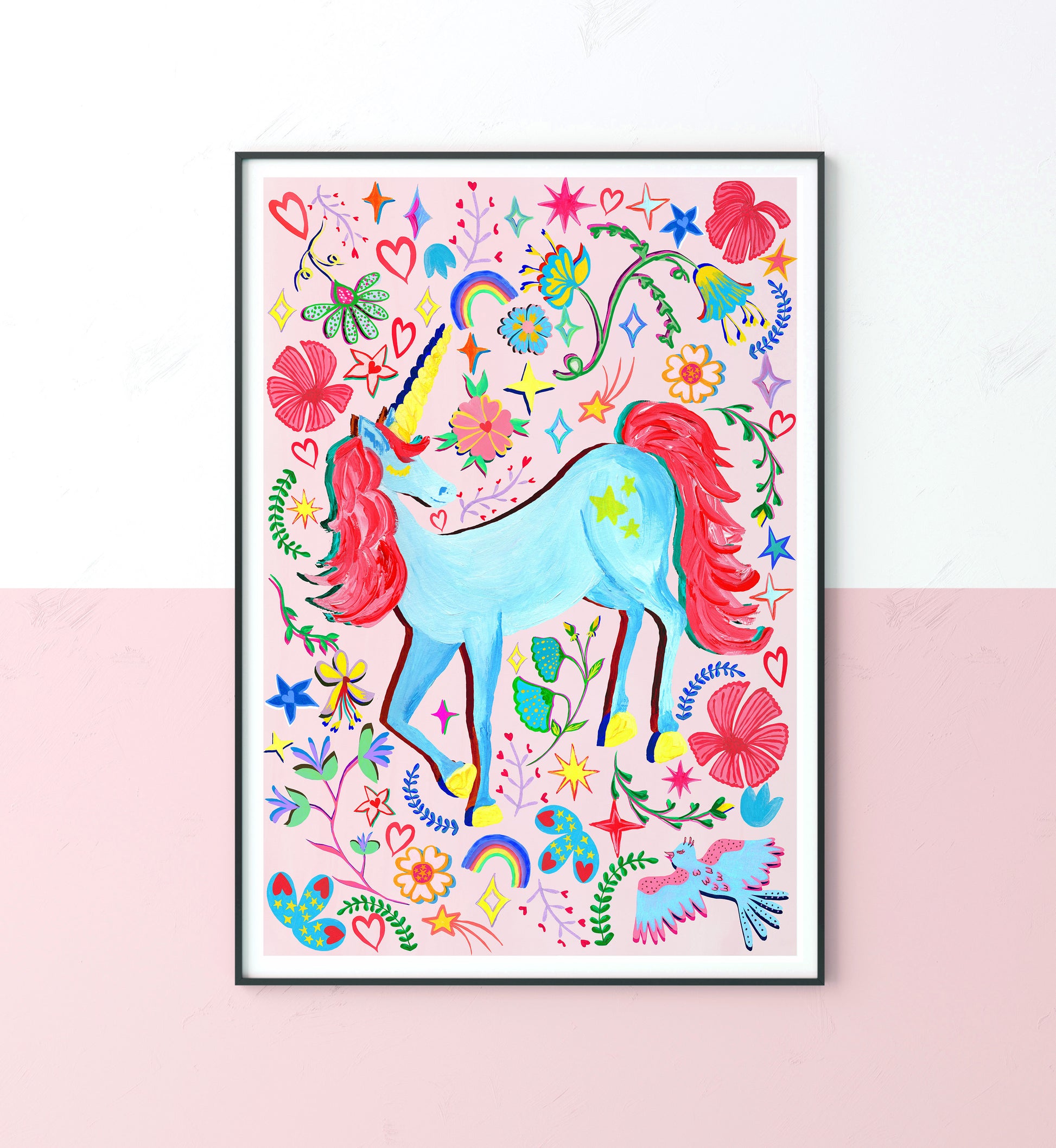 A colourful blue unicorn painting surround by colourful flowers and rainbow illustrations on a light pink background  ina black frame on a white and pink wall.