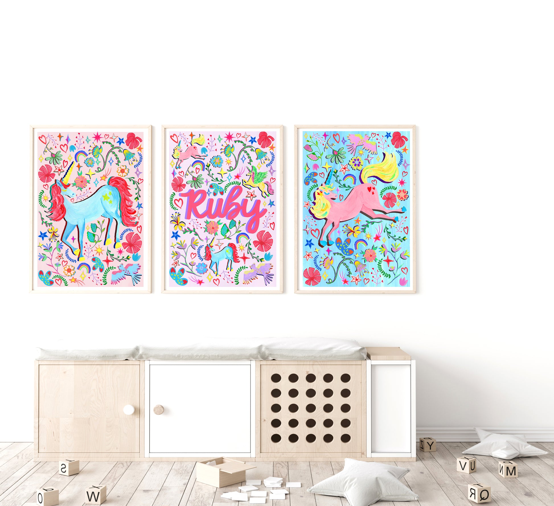 Three colorful unicorn prints with floral designs on a white wall above a wooden cabinet.