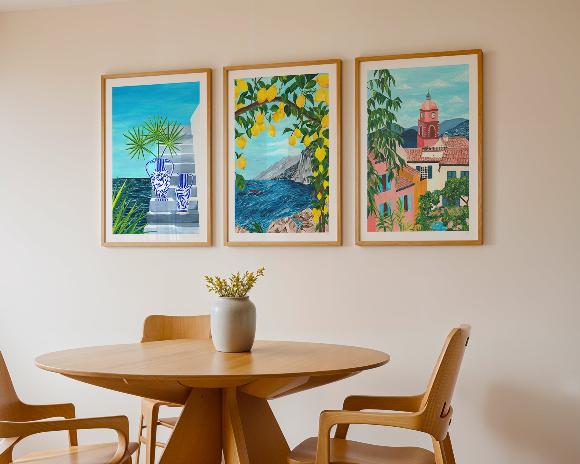 Dining room with a round wooden table and chairs, featuring three colorful framed artworks on the wall.