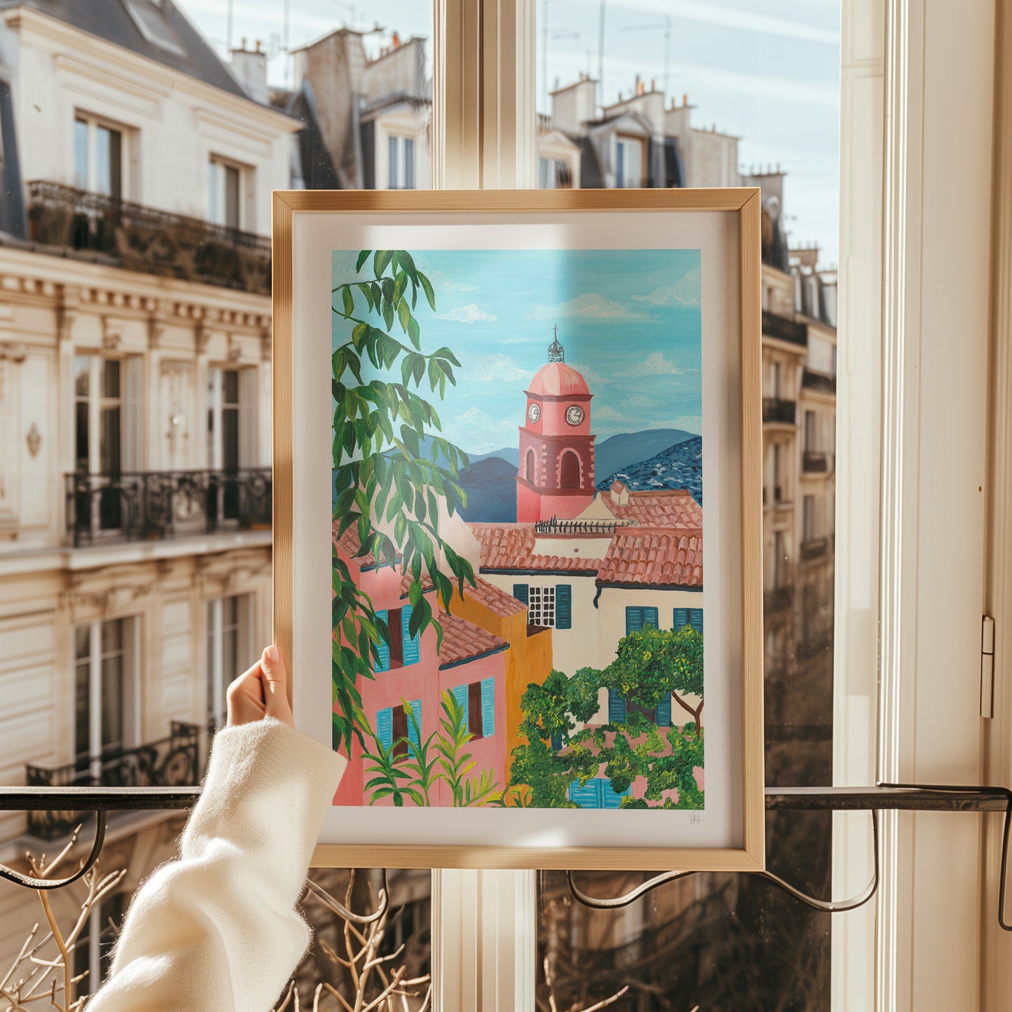 Framed artwork of a colorful cityscape held in front of a window with a view of buildings.
