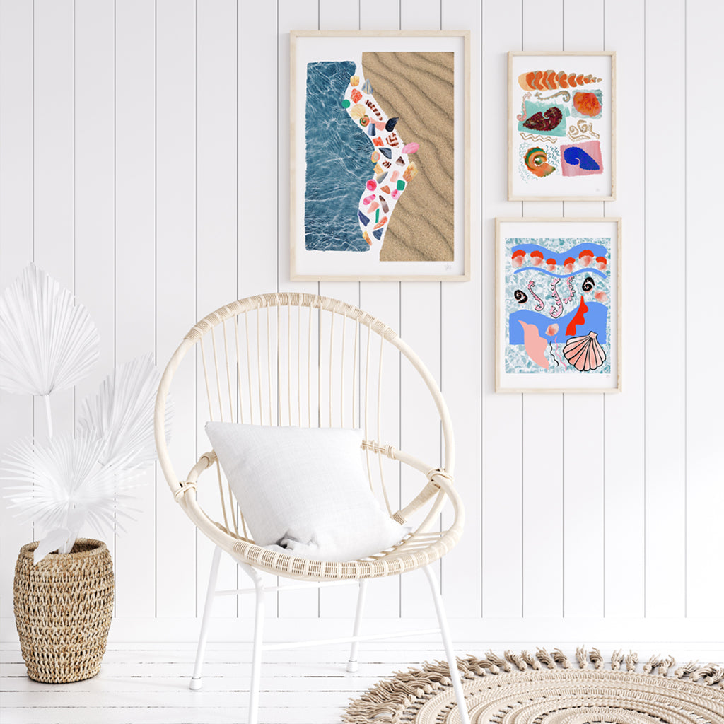 Wicker chair with a white cushion in front of a wall with three framed artworks.