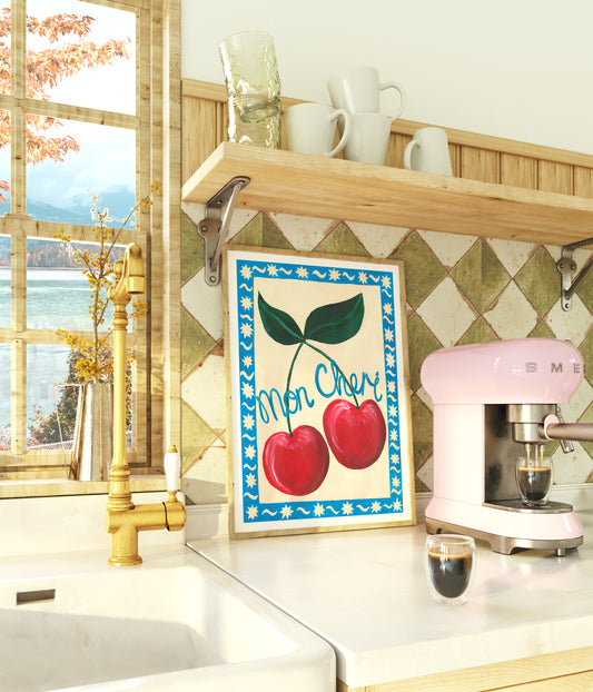Kitchen counter with a pink Smeg coffee machine, cherry-themed artwork, and window view.