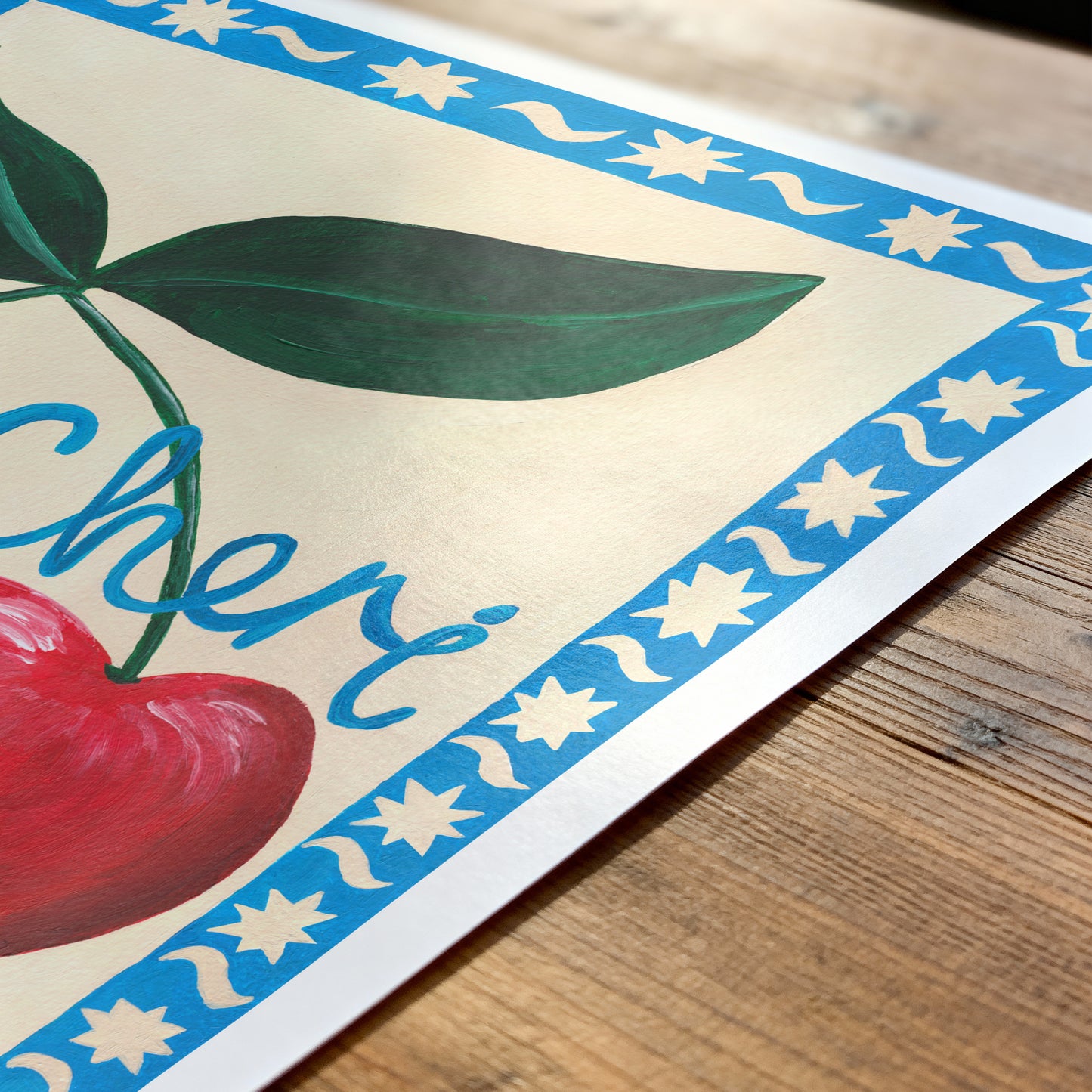 Close-up of a decorative paper with cherries and a blue border on a wooden surface