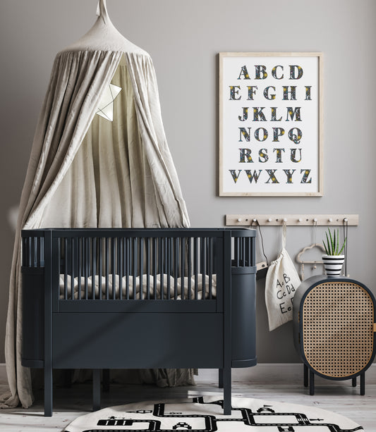 Nursery room with a black crib, decorative canopy, and alphabet poster on a gray wall.