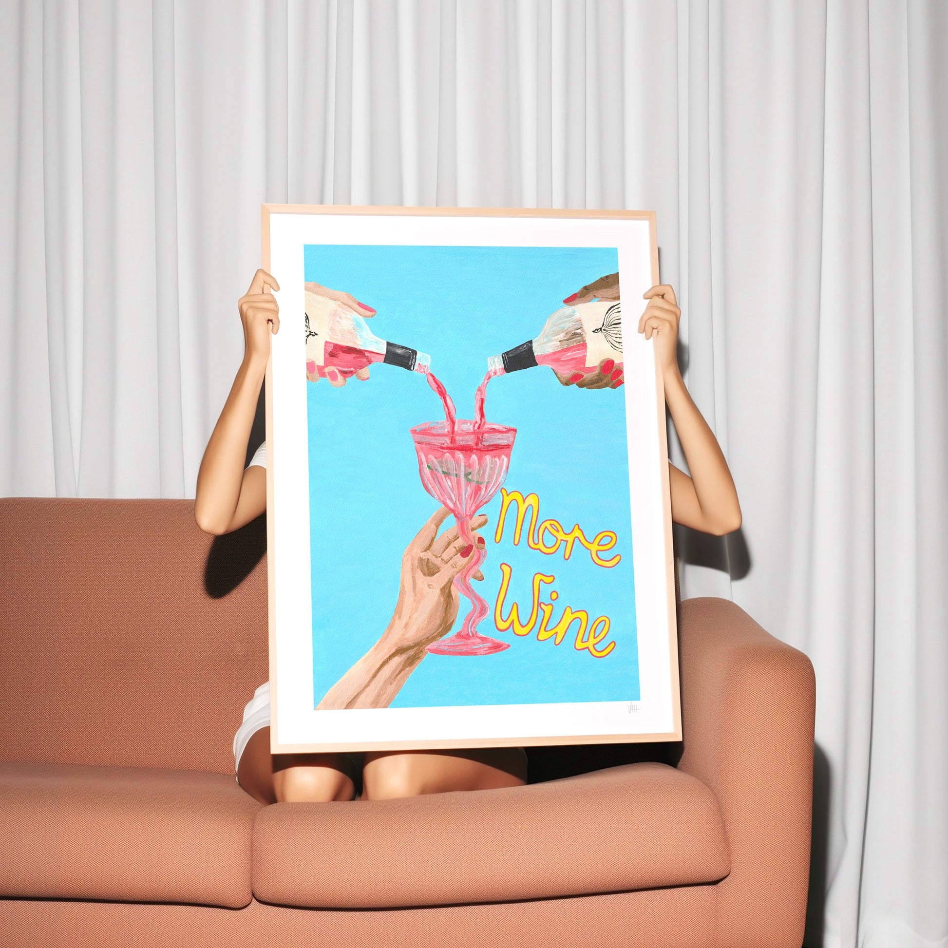 A personholding a framed poster with 'More Wine' text against a white curtain background.