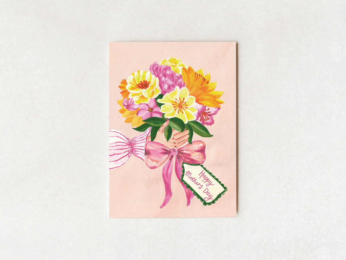 A square greeting card featuring a watercolor-style bouquet of yellow, pink, and orange flowers tied with a pink ribbon and a small tag that reads 'Happy Mother's Day,' shown against a light neutral background.