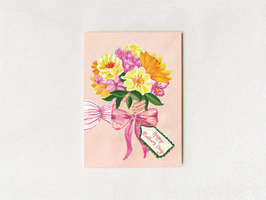 A square greeting card featuring a watercolor-style bouquet of yellow, pink, and orange flowers tied with a pink ribbon and a small tag that reads 'Happy Mother's Day,' shown against a light neutral background.