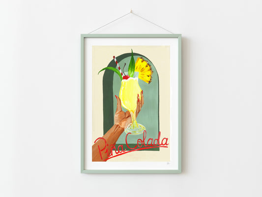 Framed artwork of a hand holding a yellow cocktail with 'Pina Colada' text on a white wall.