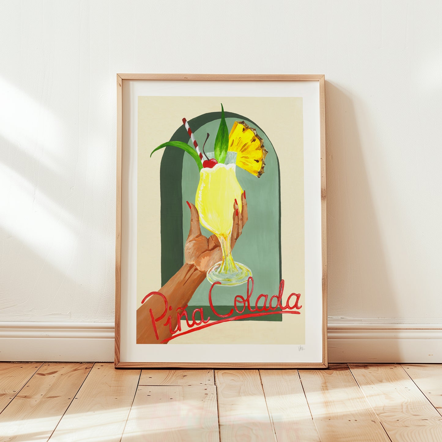 Framed artwork of a hand holding a Pina Colada with a pineapple garnish on a light wooden floor.