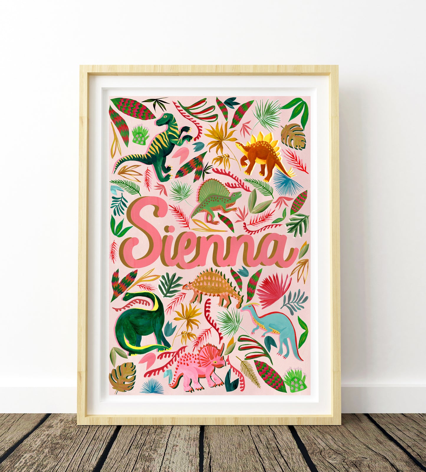 Framed artwork with colorful dinosaur illustrations and the name 'Sienna' on a light background.