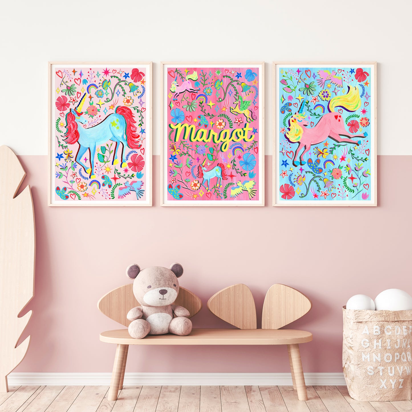 Three colorful unicorn posters on a pink wall with a wooden bench and teddy bear.