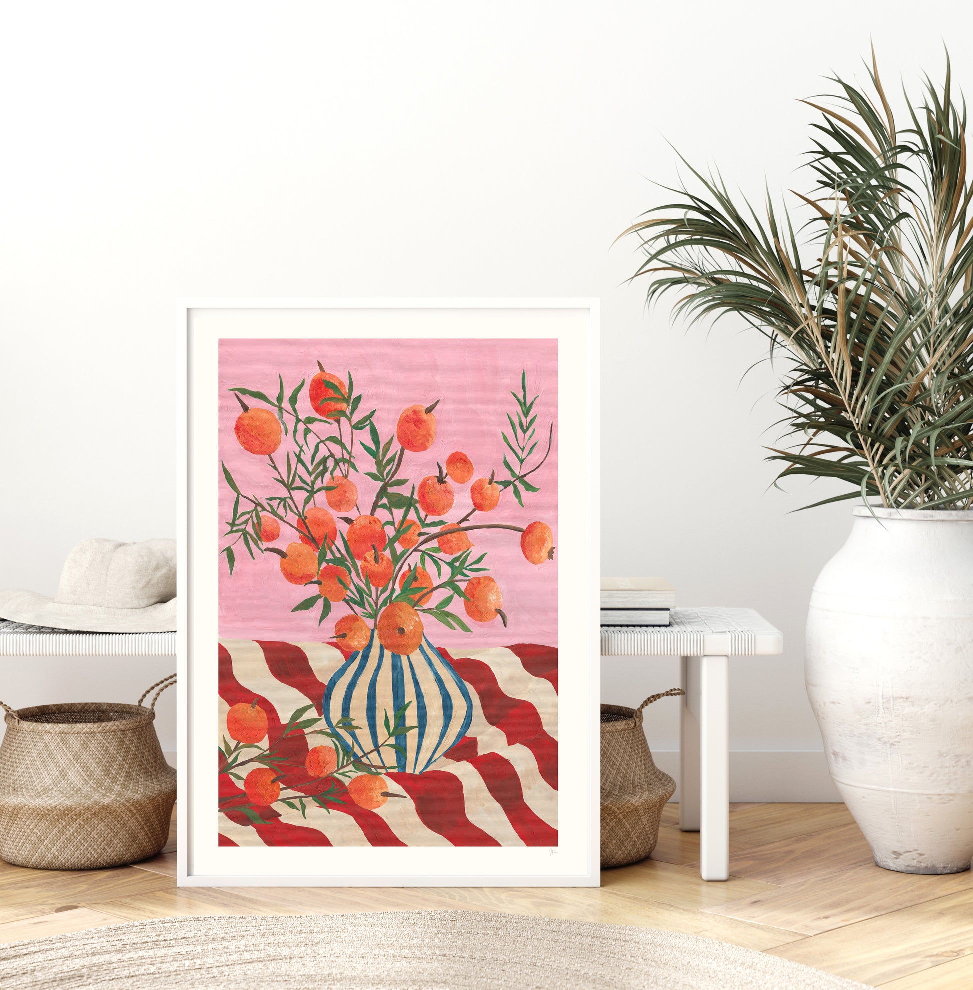 Framed artwork with a fruit in a vase design on a pink background in a room with a plant and furniture.