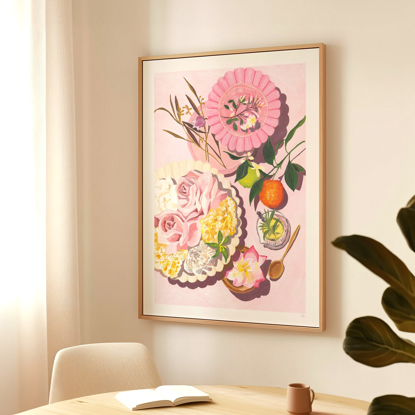 Framed floral artwork on a wall above a table with a book and mug.