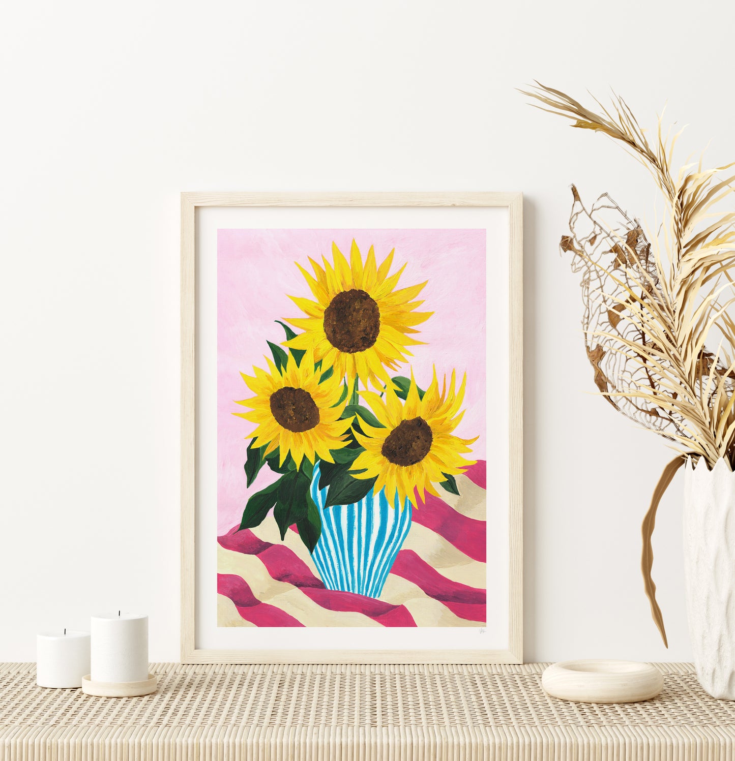 Framed artwork of sunflowers on a pink background, displayed on a table with decorative elements.