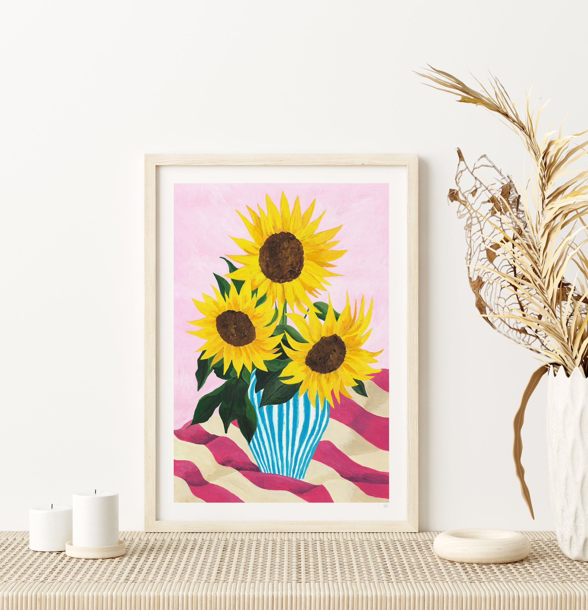 Framed artwork of sunflowers on a pink background, displayed on a table with decorative elements.