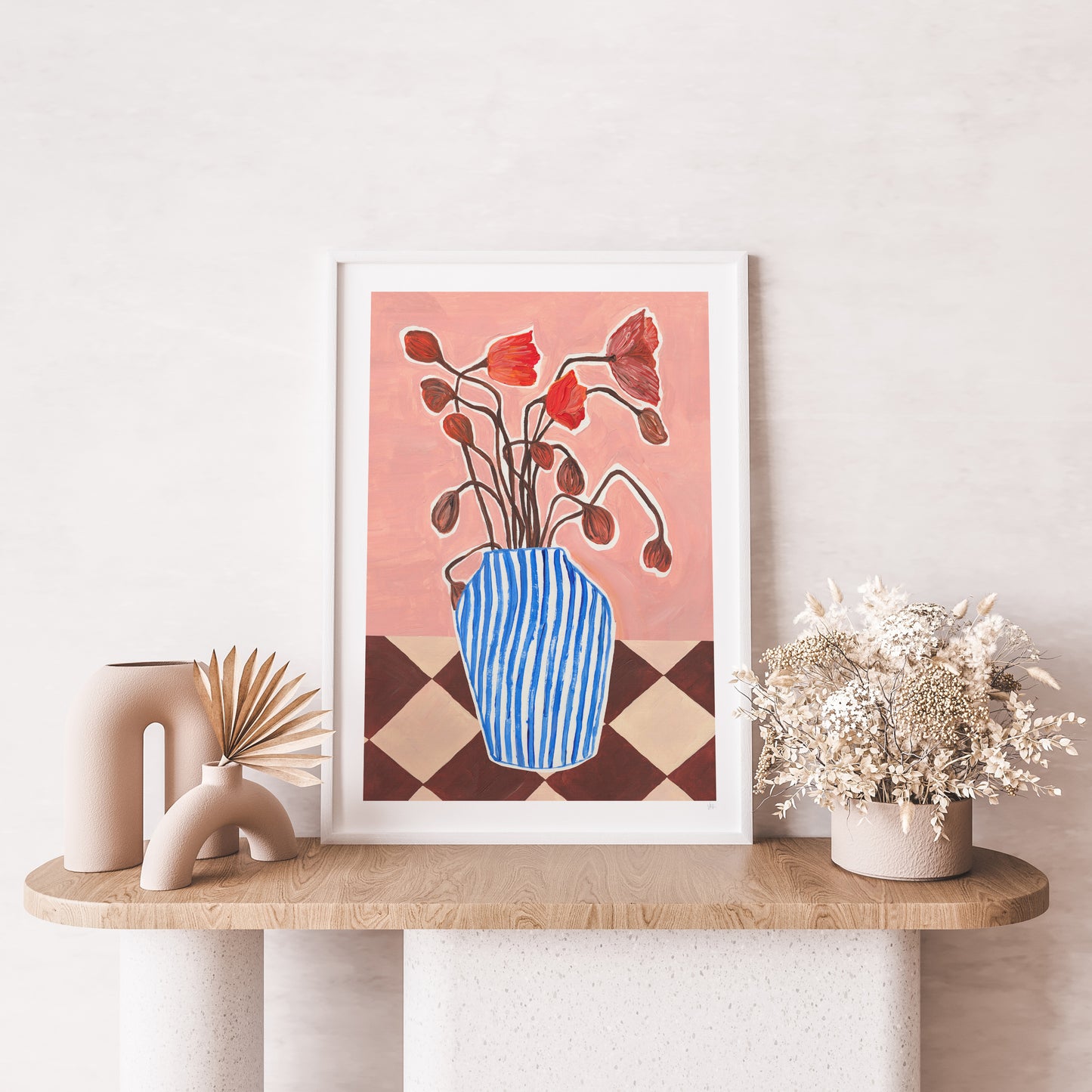 Framed artwork of a vase with flowers on a wooden shelf against a white wall.