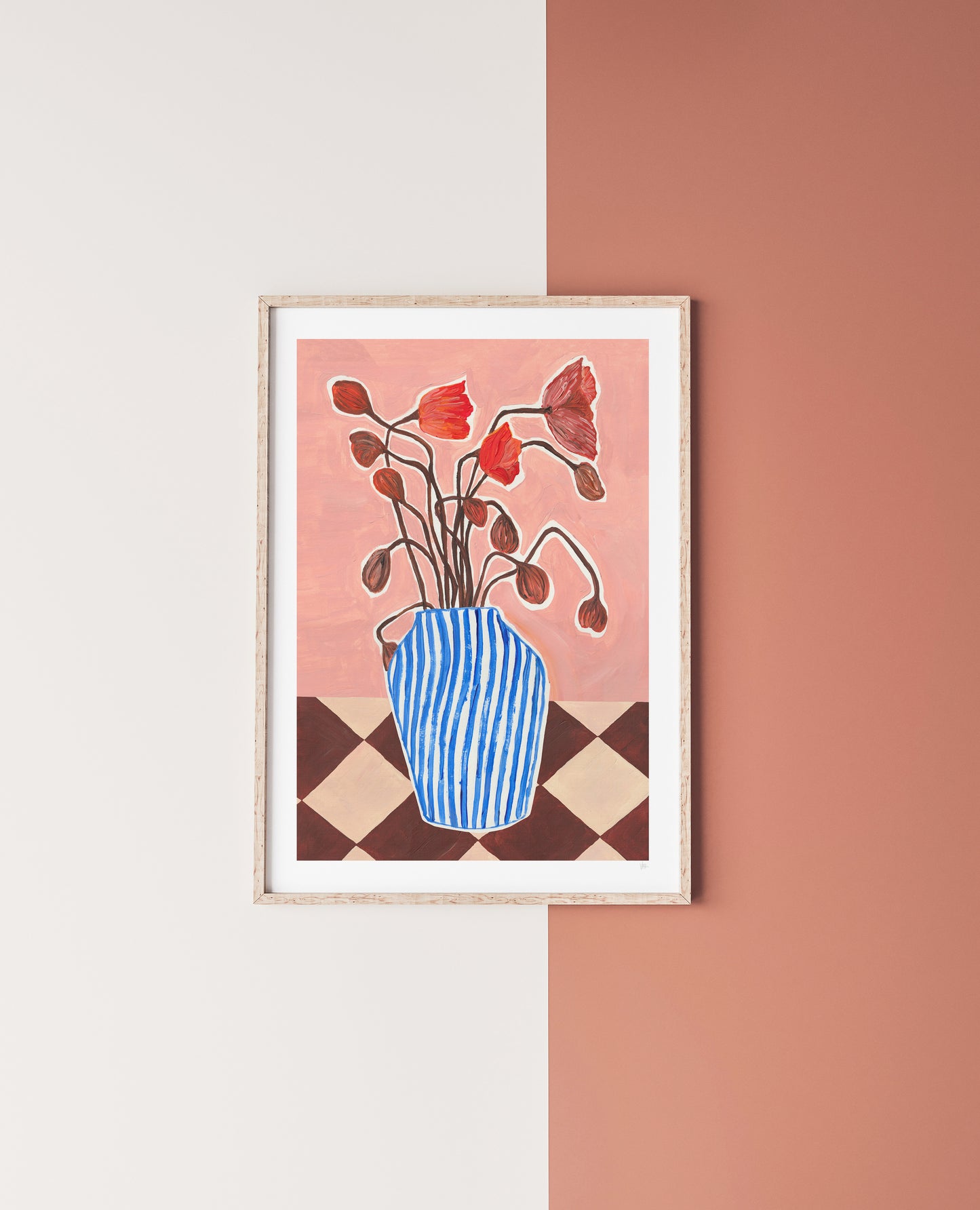 Framed artwork of a blue vase with red flowers on a checkered tablecloth against a two-tone wall.