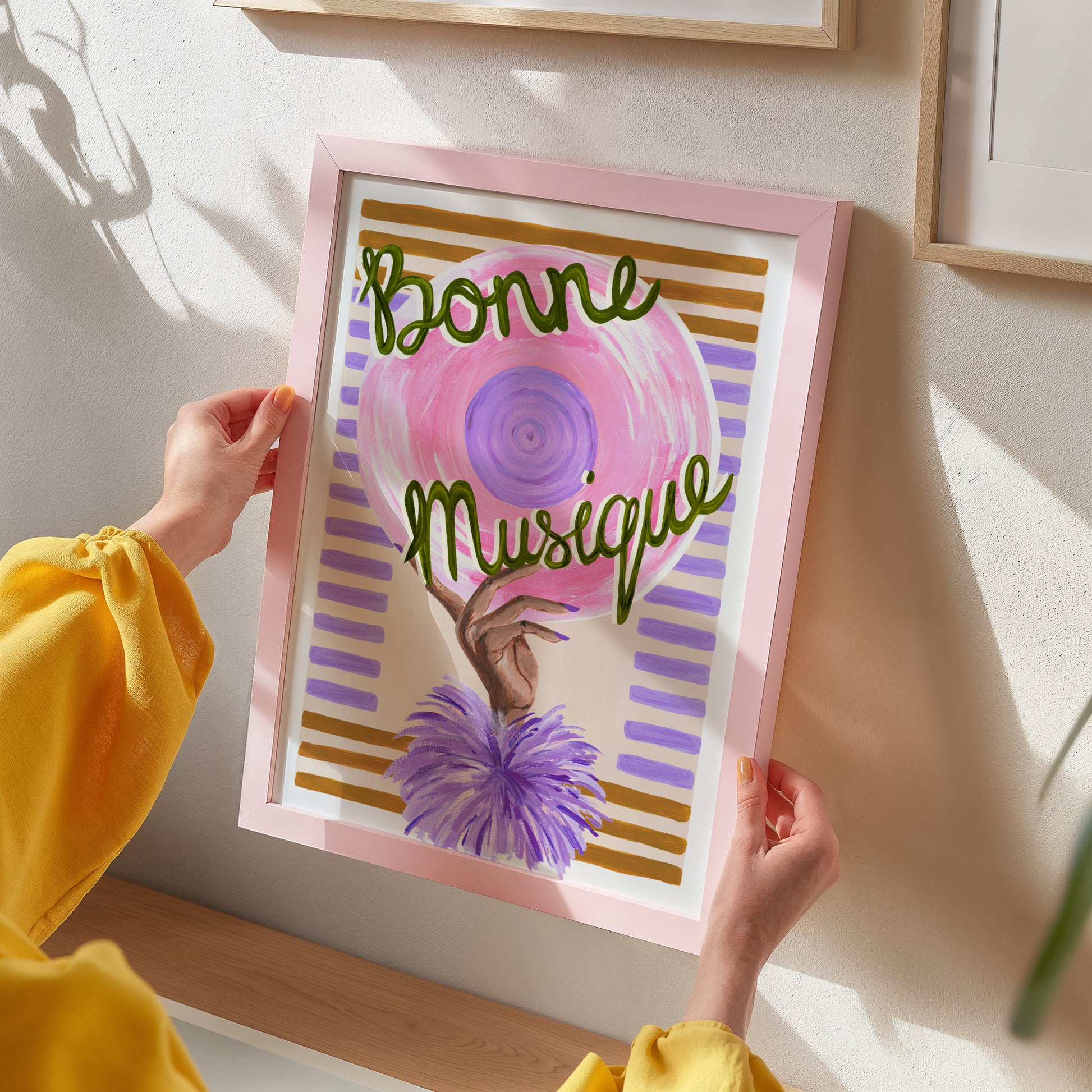 Person holding a framed artwork with 'Bonne Musique' text and colorful design.