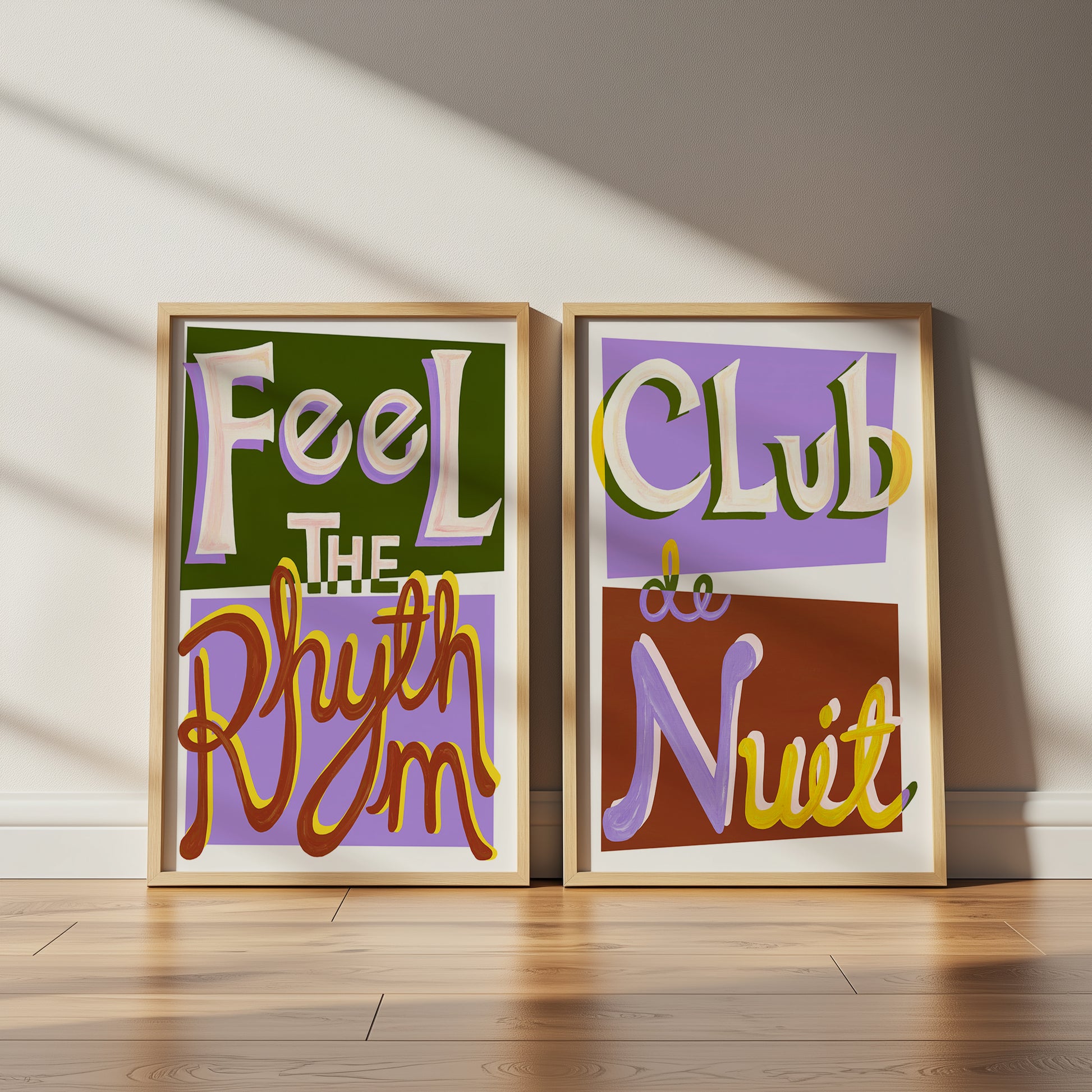 Two framed posters with colorful text on a wooden floor and light-colored wall.