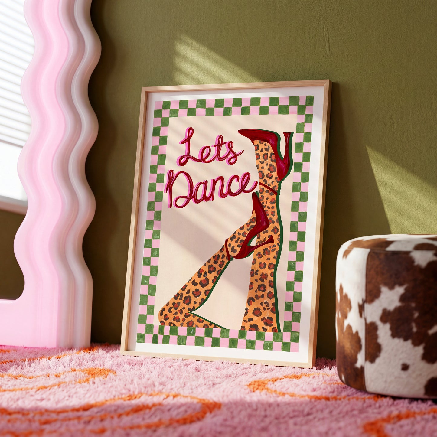 Framed artwork with 'Let's Dance' text and leopard print shoes on a checkered background, placed on a pink surface.