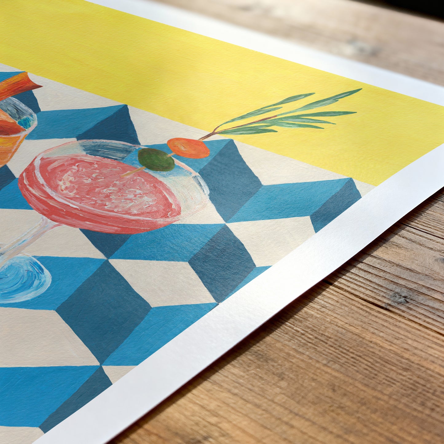 Colorful illustration of a cocktail on a geometric patterned paper, placed on a wooden surface.