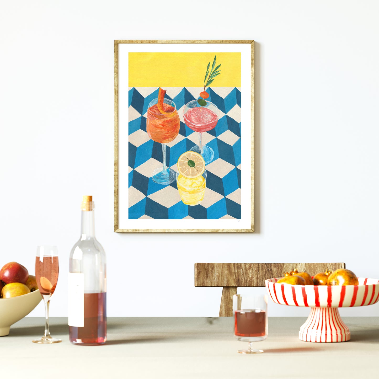 Framed artwork of cocktails on a wall with a table setup below