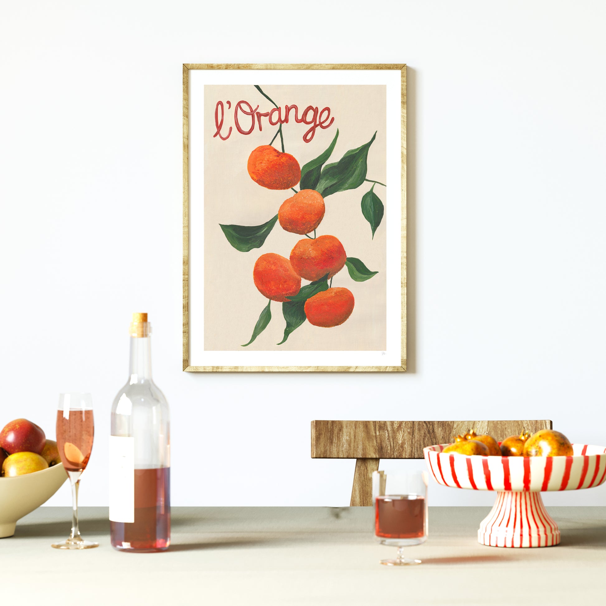 Framed artwork of oranges with 'L'Orange' text above a table setting with wine and fruit.