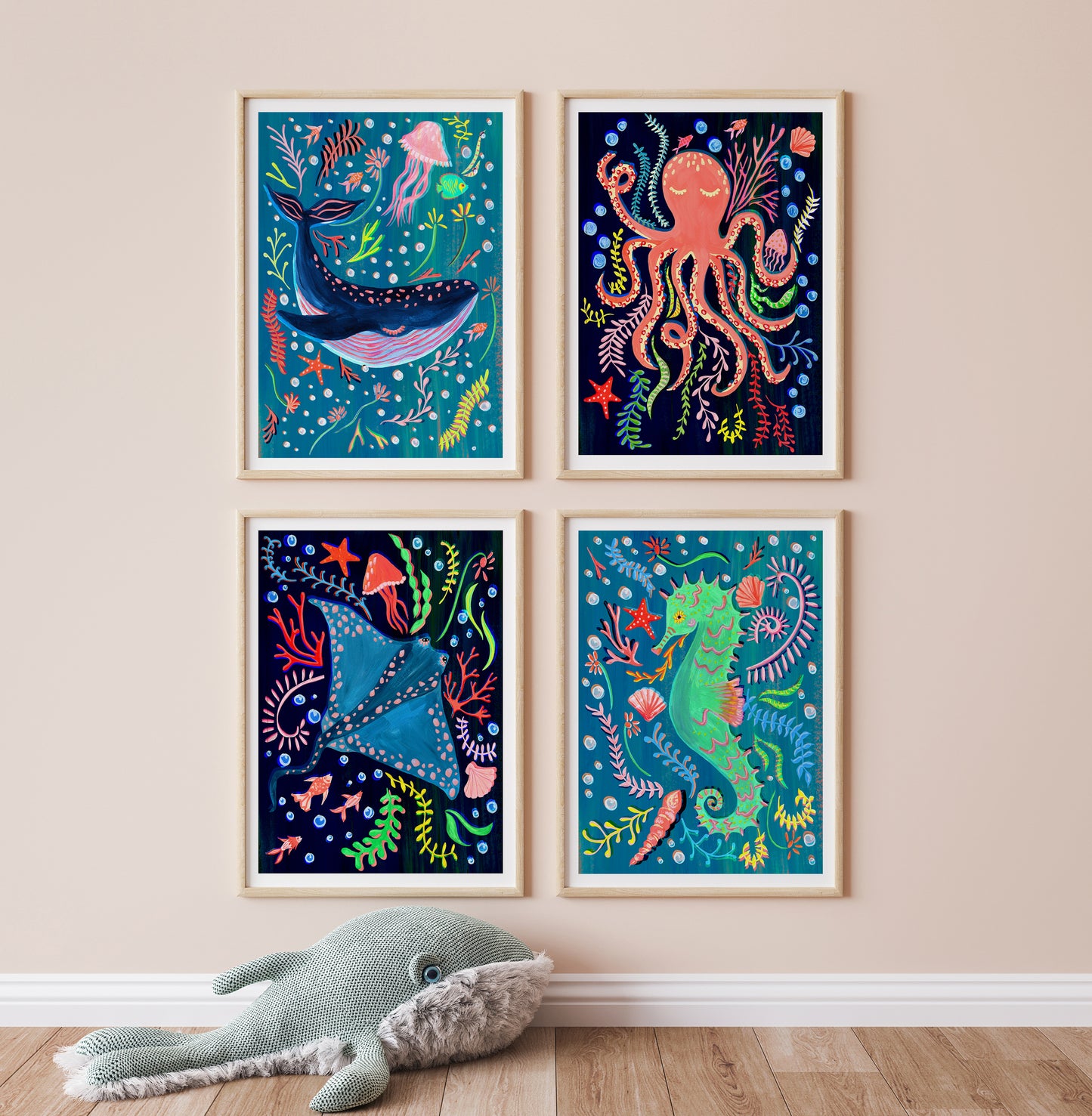 Four colorful framed illustrations of marine animals on a wall with a plush toy whale on the floor.
