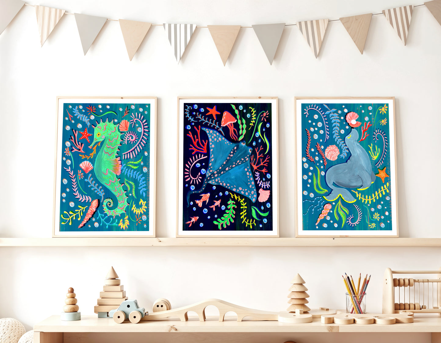 Three colorful framed artworks of sea creatures on a shelf with wooden toys below.