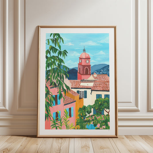 Framed artwork of a colorful village scene with a clock tower on a wall.