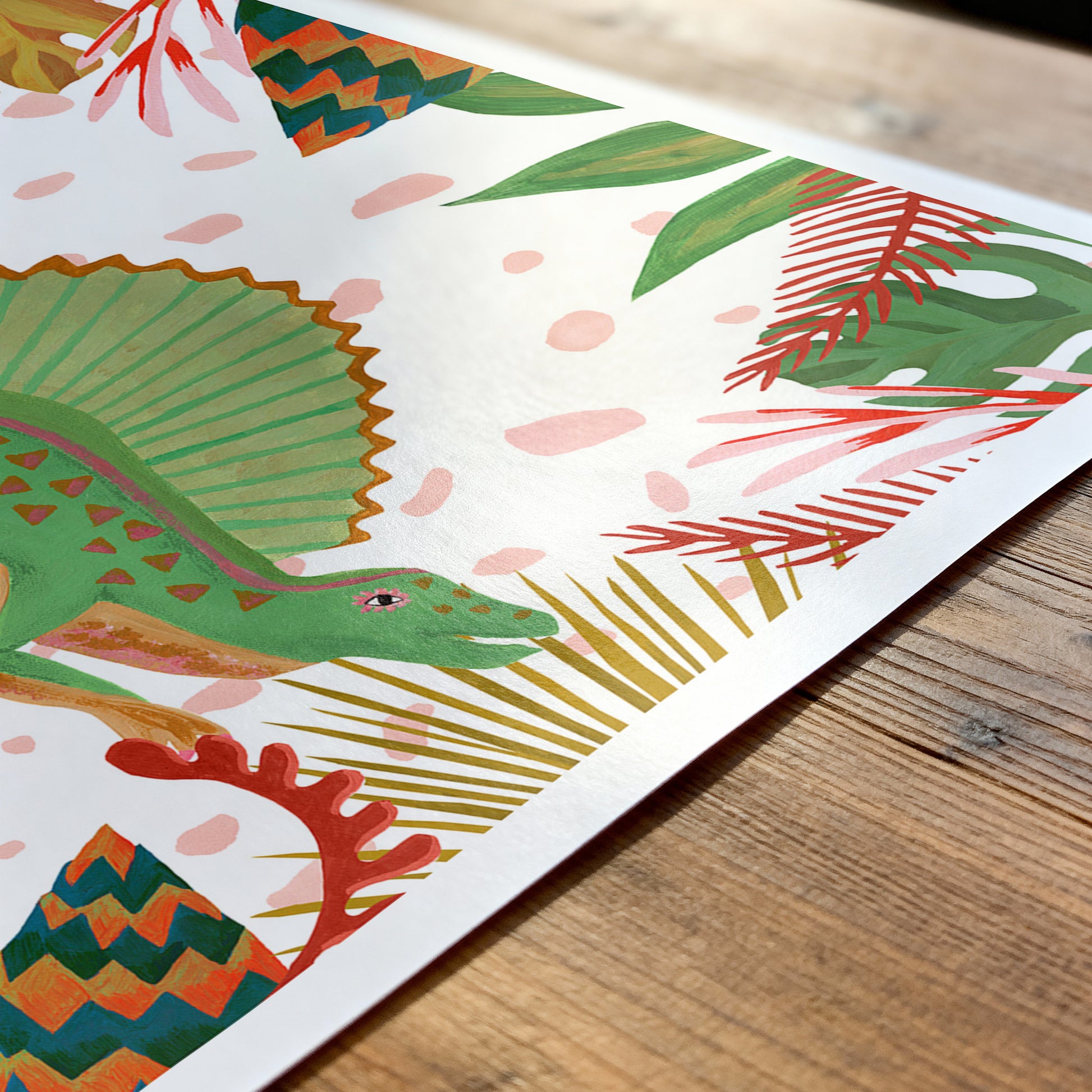 Colorful dinosaur illustration on a white background with green leaves and red flowers, placed on a wooden surface.