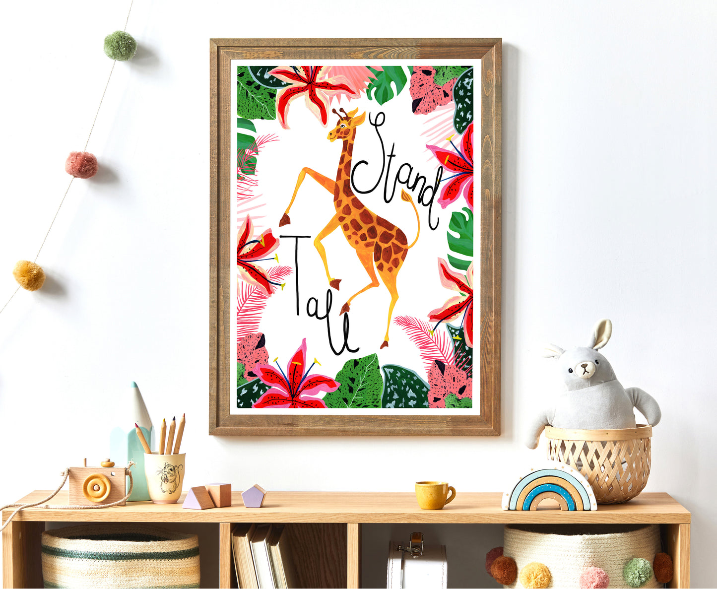 Framed artwork with a giraffe illustration and floral elements on a wall above a shelf.