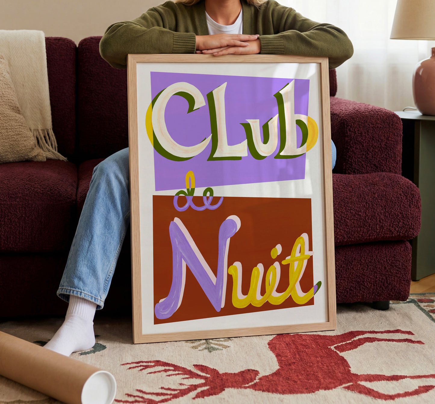Person holding a framed sign with 'Club de Nuit' text in a living room setting