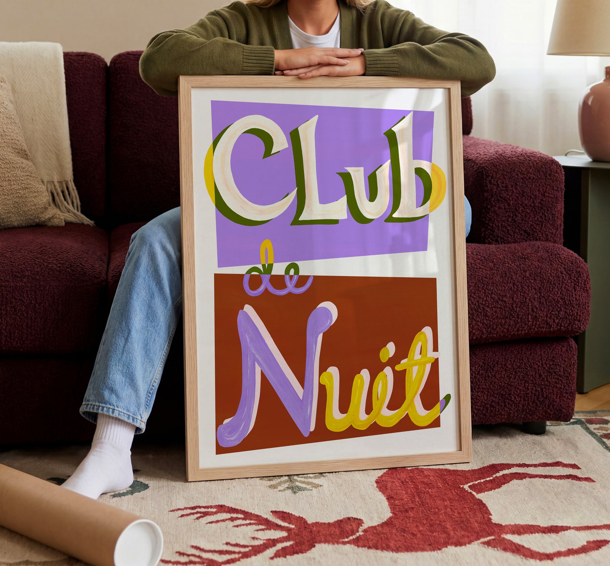 Person holding a framed sign with 'Club de Nuit' text in a living room setting
