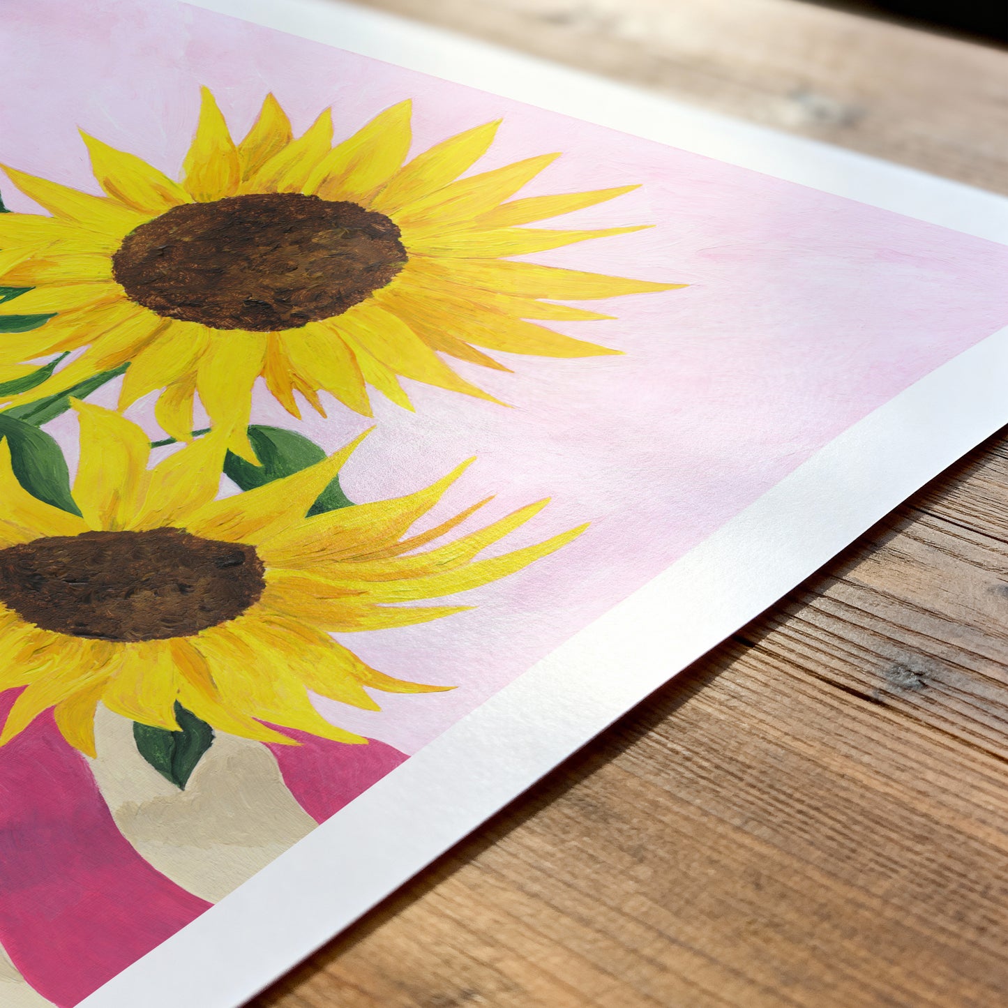 Two sunflowers on a pink background with a wooden surface below