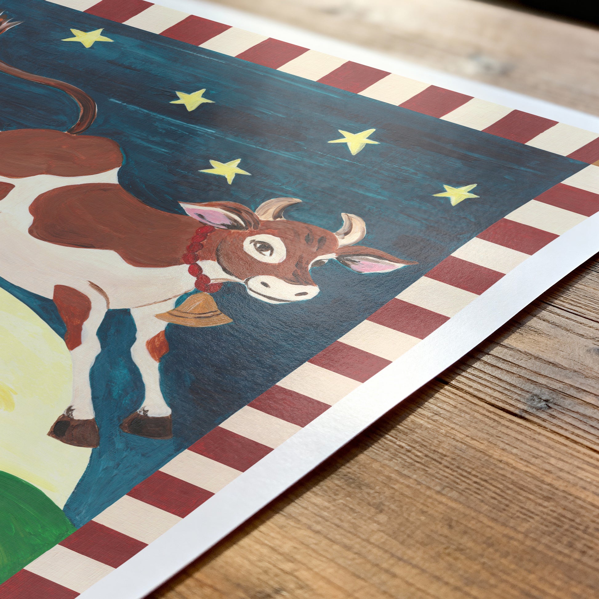 Children's illustration of a cow with stars and a striped border on a wooden surface
