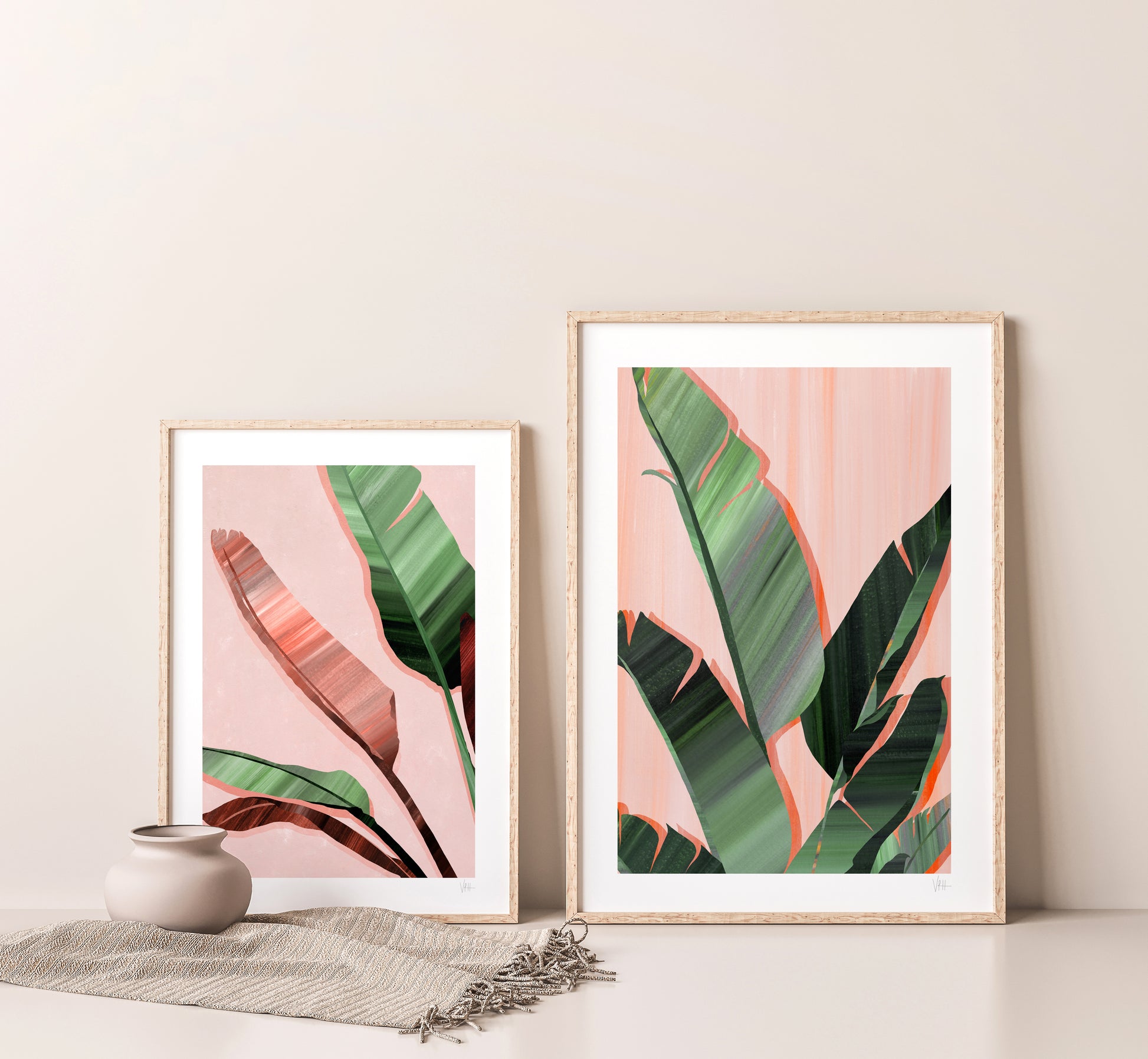 Two framed prints of tropical leaves on a light pink background, displayed on a neutral wall.