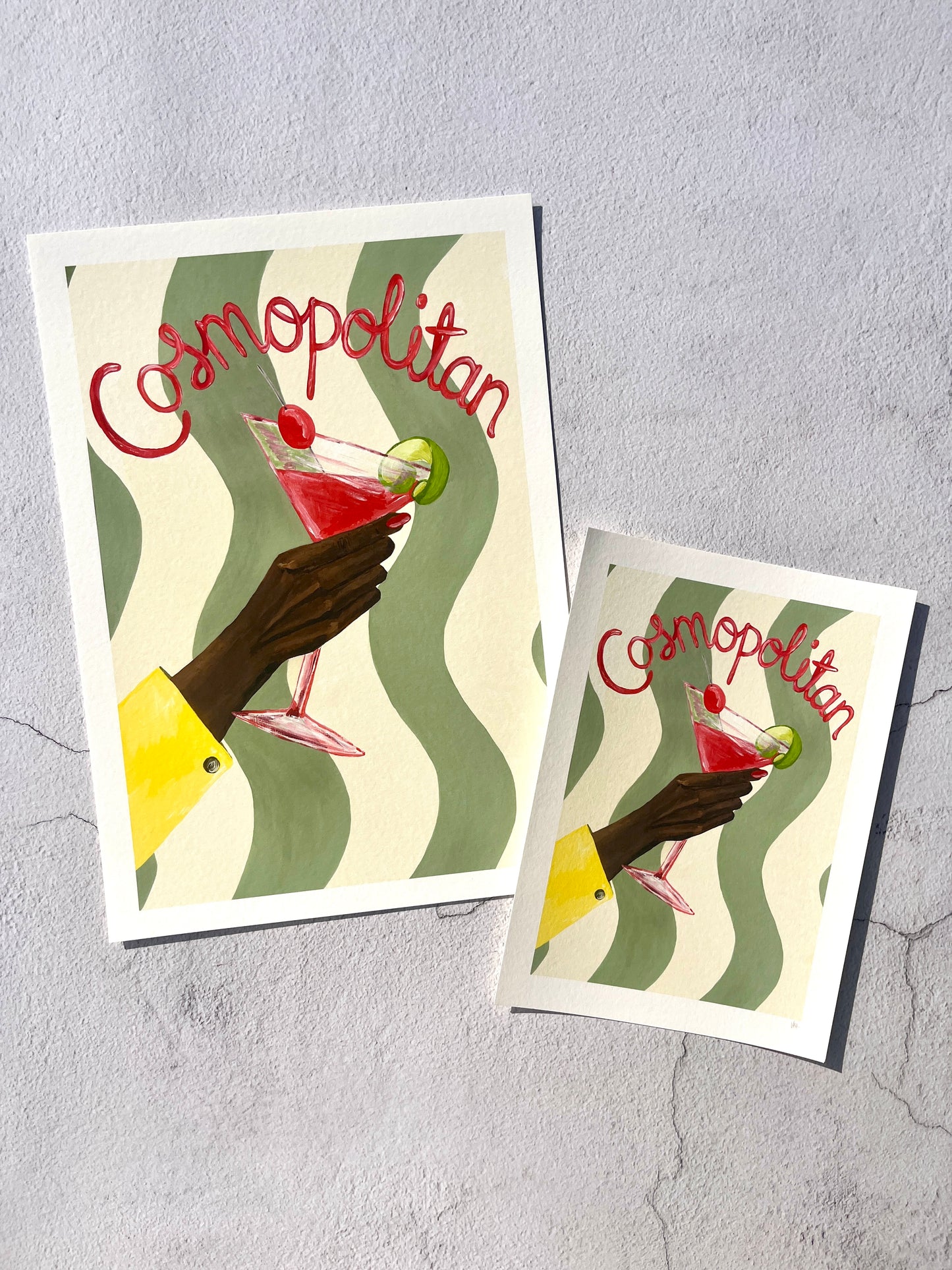 Two 'Cosmopolitan' cocktail cards with a hand holding a drink against a wavy patterned background.