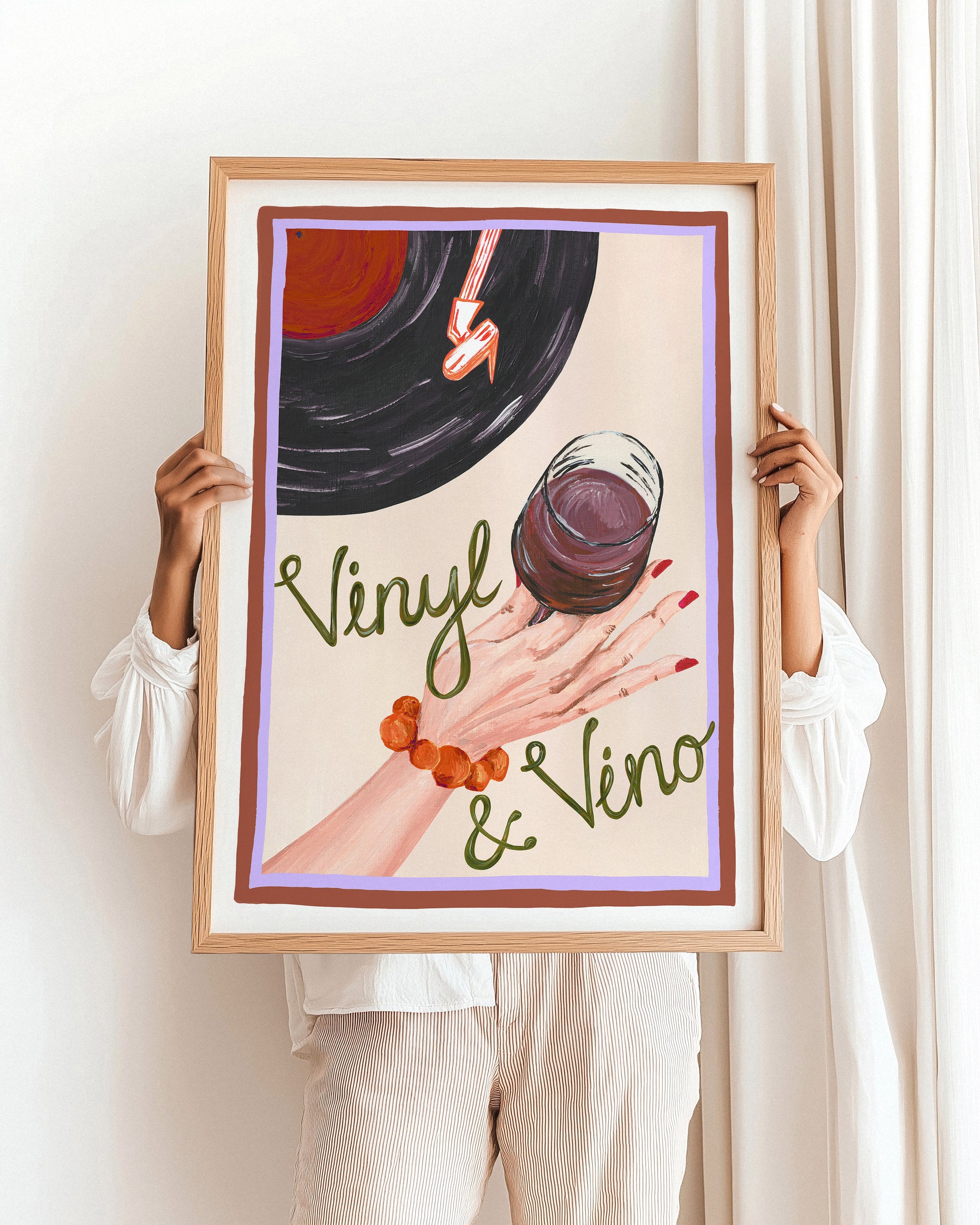 Person holding a framed artwork with a vinyl record and glass of red wine.