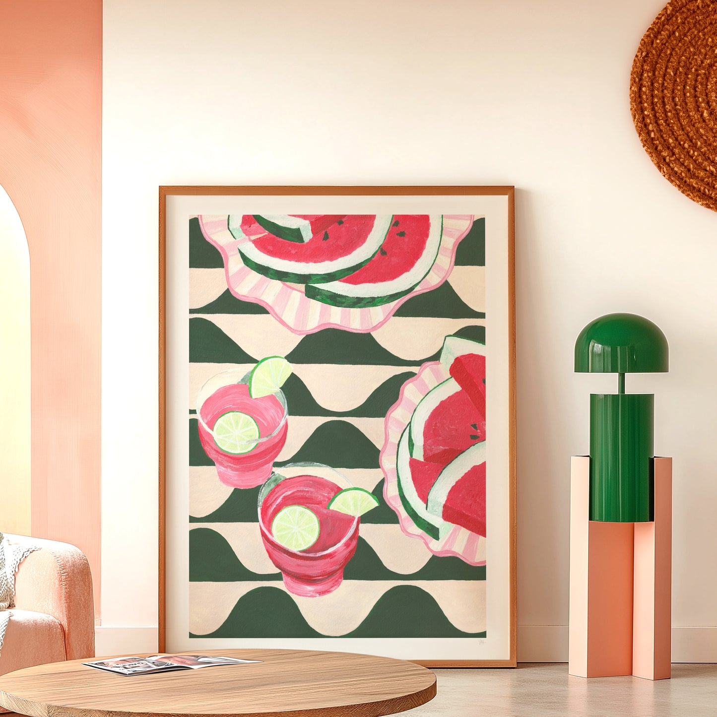 Framed artwork with watermelon and cocktail design in a room with a pink wall and wooden table.
