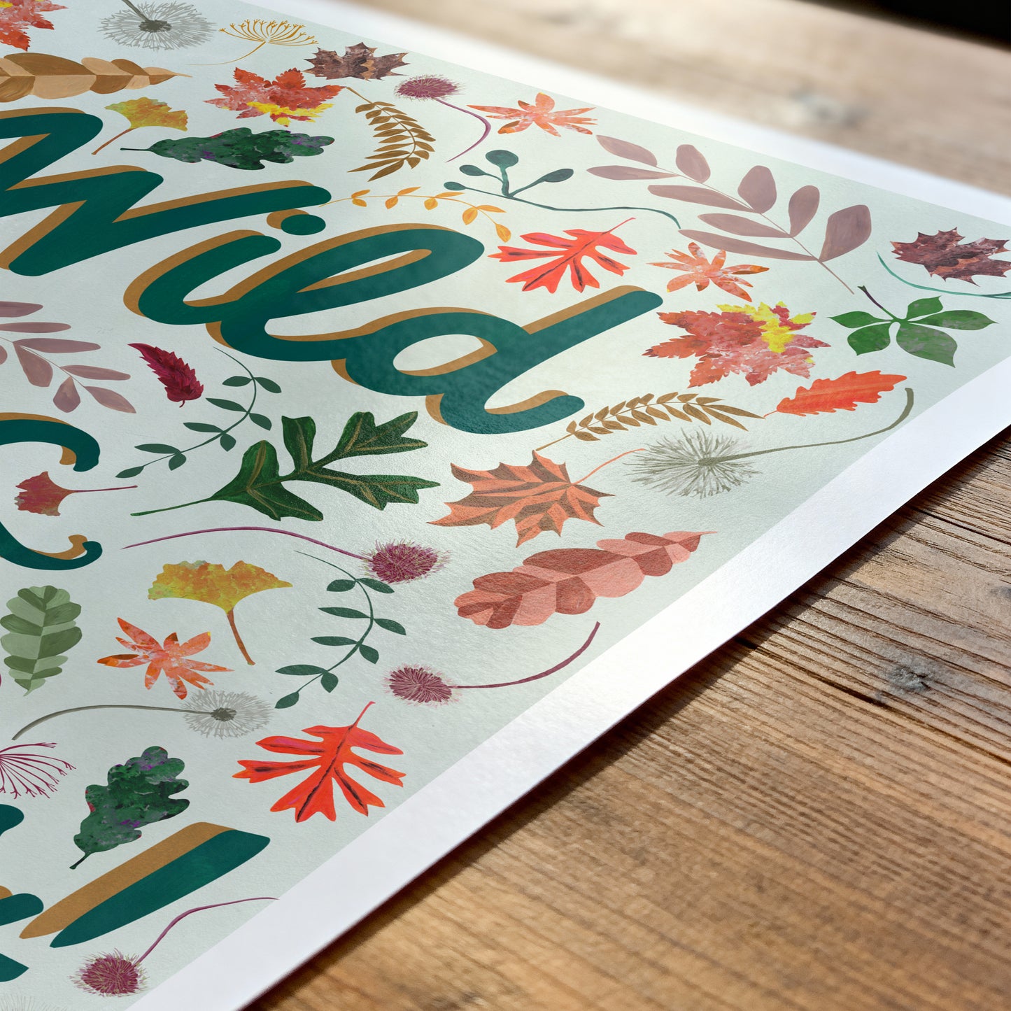Colorful autumn leaf design with the words 'wild & Curious' on a wooden surface