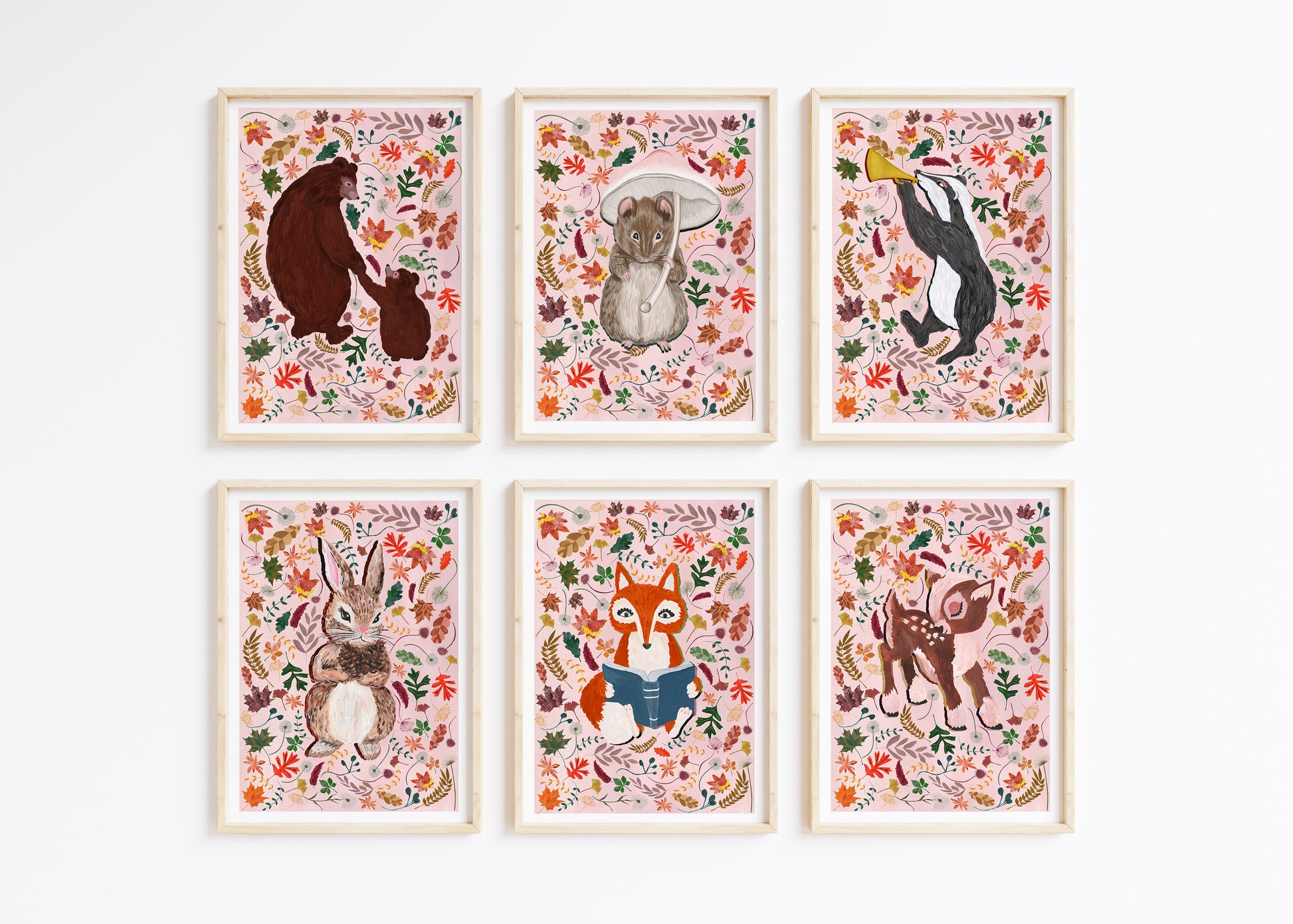 A set of 6 woodland animal prints, of a bear, mouse, badger, rabbit, fox and deer suurounds by autumn leaves on a pale pink background, framed on a white wall