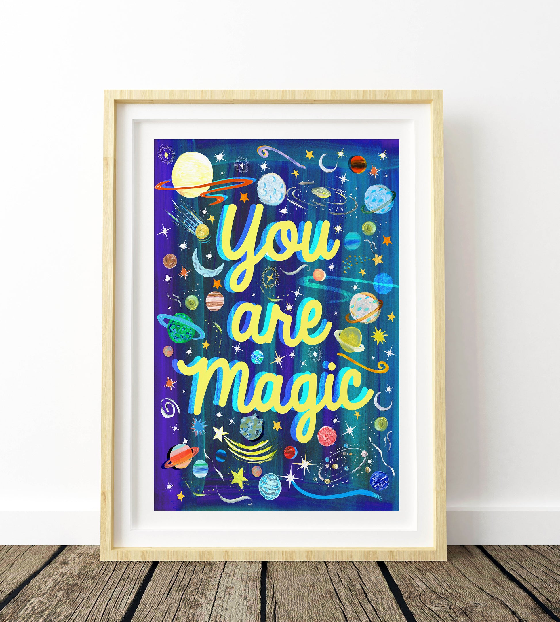 Framed artwork with 'You are Magic' text and space-themed design on a wooden floor.