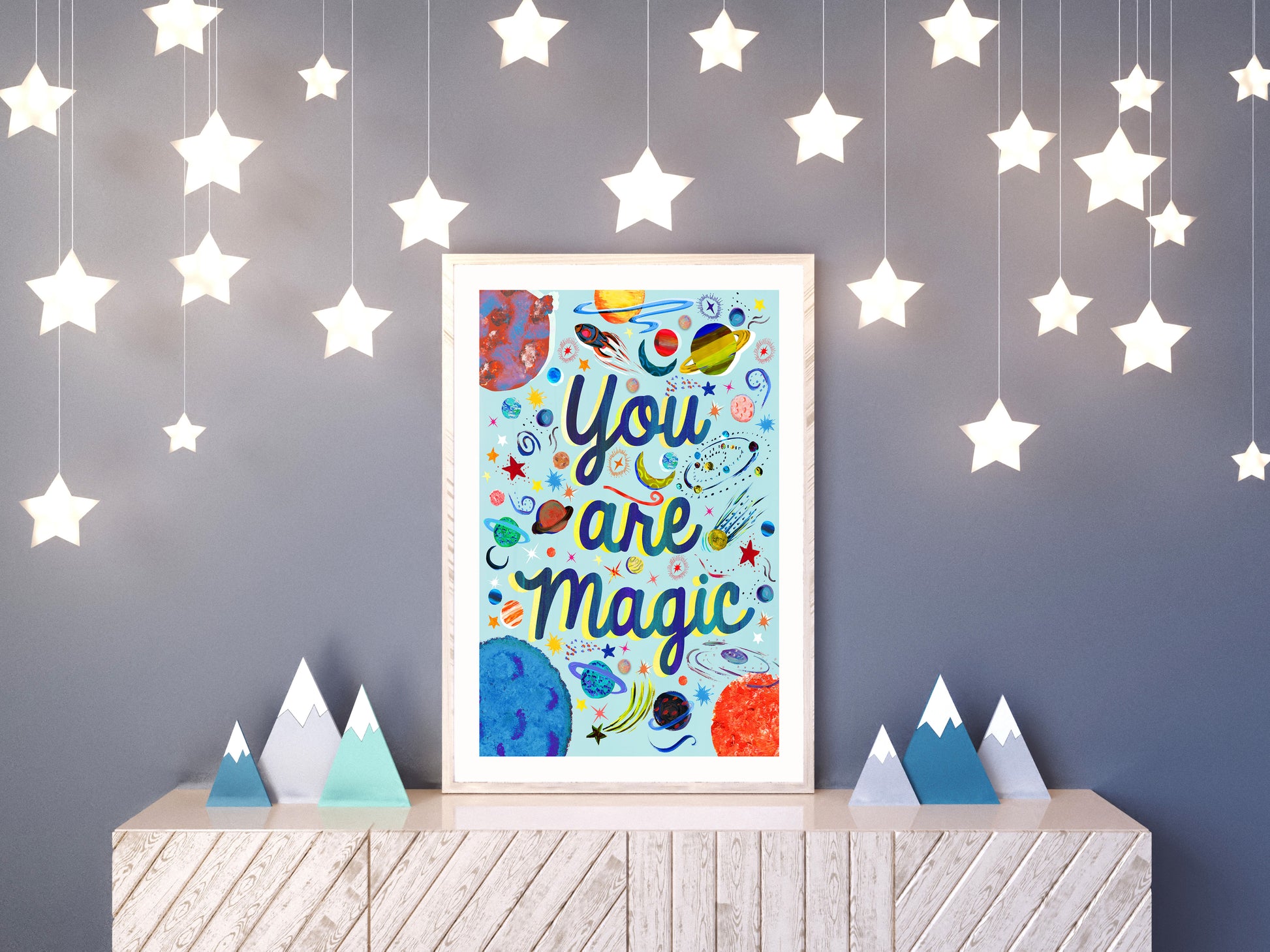 a light up star decorated room displaying a space illustration artwork of planets and stars with the words 'you are Magic' on top pf a cupboard with wood mountain decor