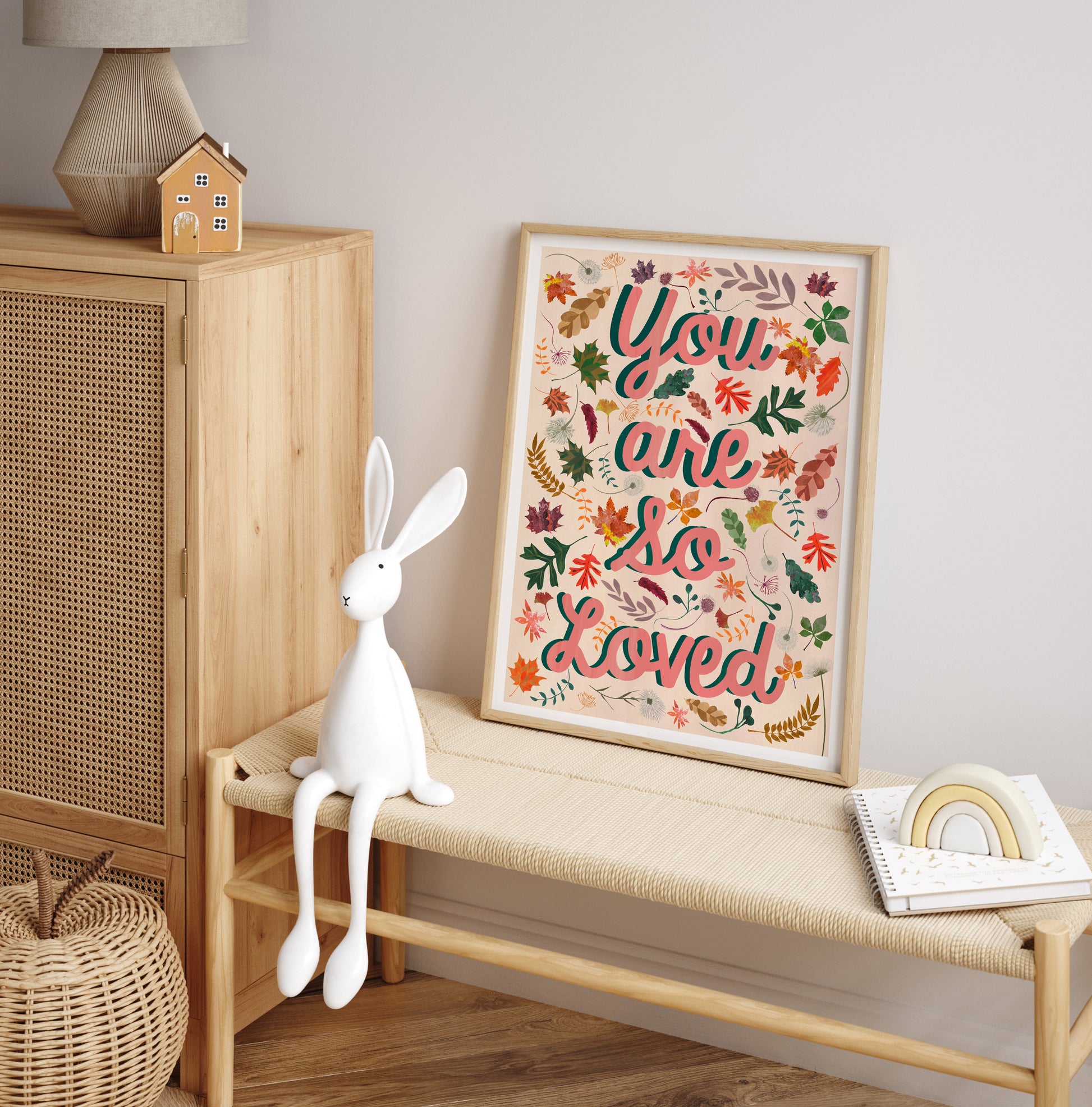 Decorative scene with a framed 'You are so loved' print, white rabbit toy, and wooden cabinet.