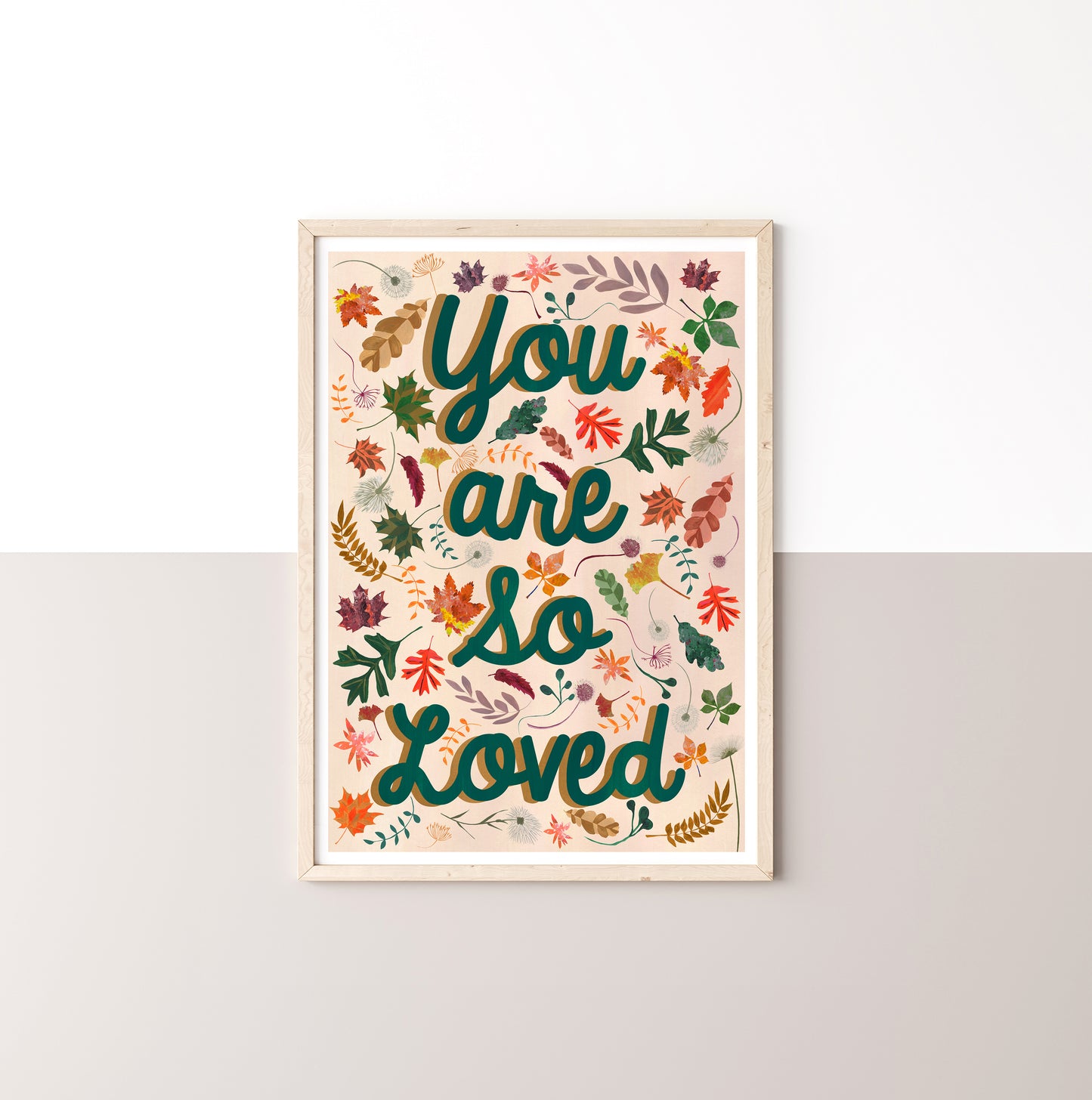 Framed artwork with 'You are so loved' text and autumn leaves designs on a white wall.